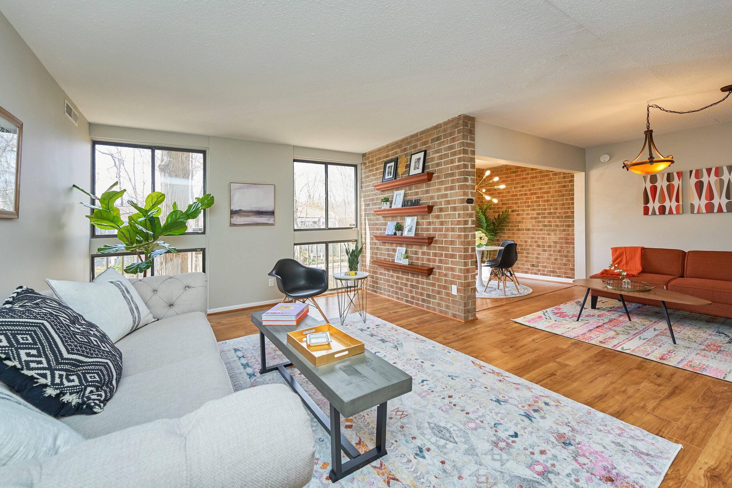 condo in Reston, Virginia showing a beautifully staged living area with hardwood floors, brick dividing wall and tasteful furniture, with lots of light from the windows