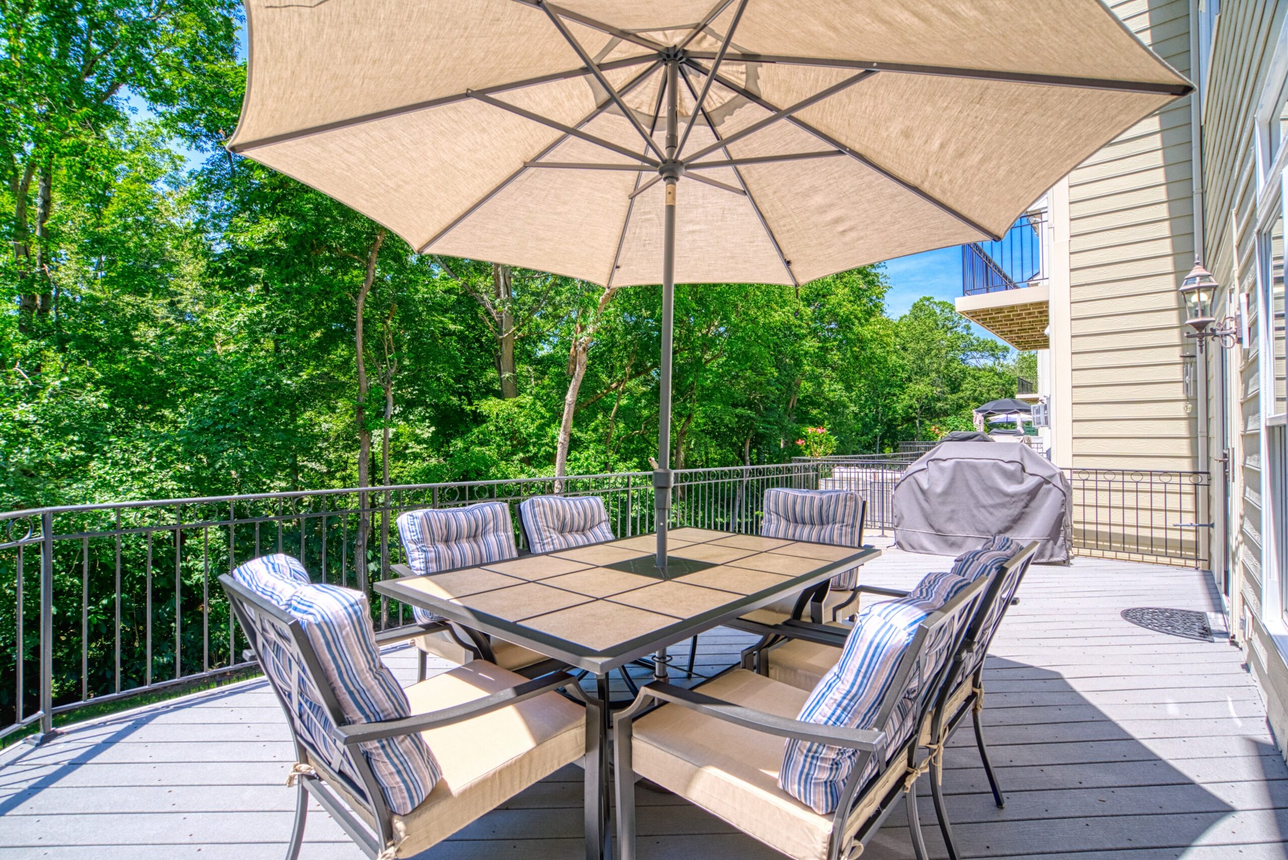 Large deck on main floor of 3-story townhome with large patio furniture and umbrella on a sunny day