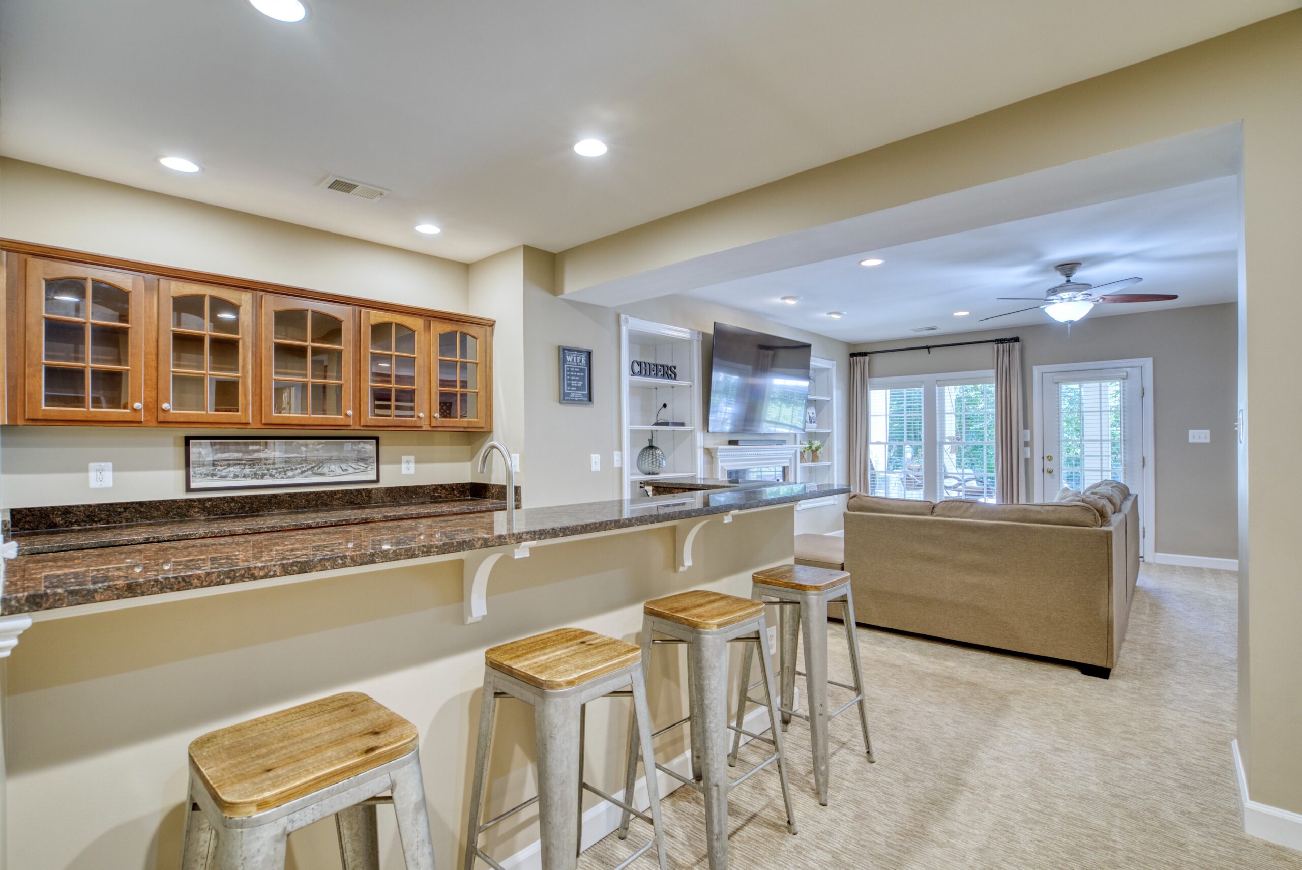 Basement wet bar in 3-story townhome with brown granite countertops and barstools, looking into the living area
