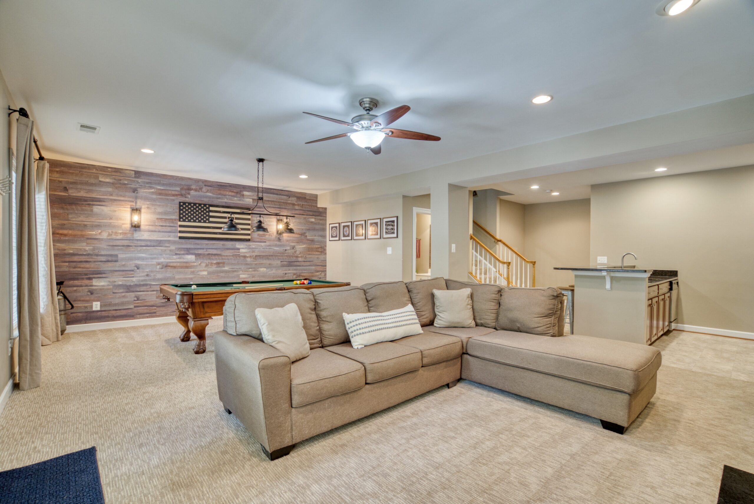 Basement living area in 3-story townhome showing large sectional couch, pool table behind and statement shiplap wall