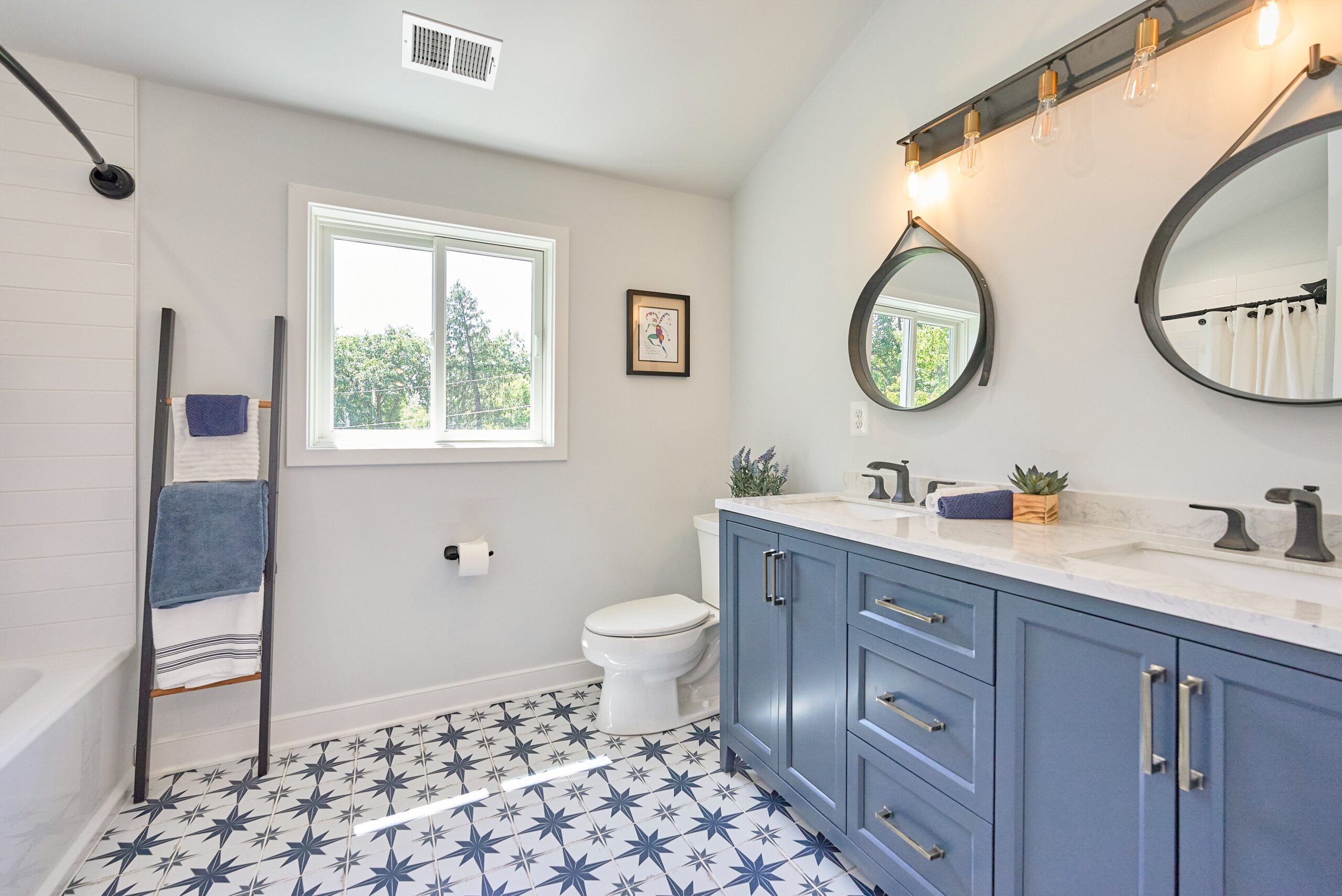 Professional photo of interior of custom home in Falls Church, Virginia. Shows remodeled bathroom with intricate tilework on the floor and dual vanities with white/grey/soft blue color scheme.