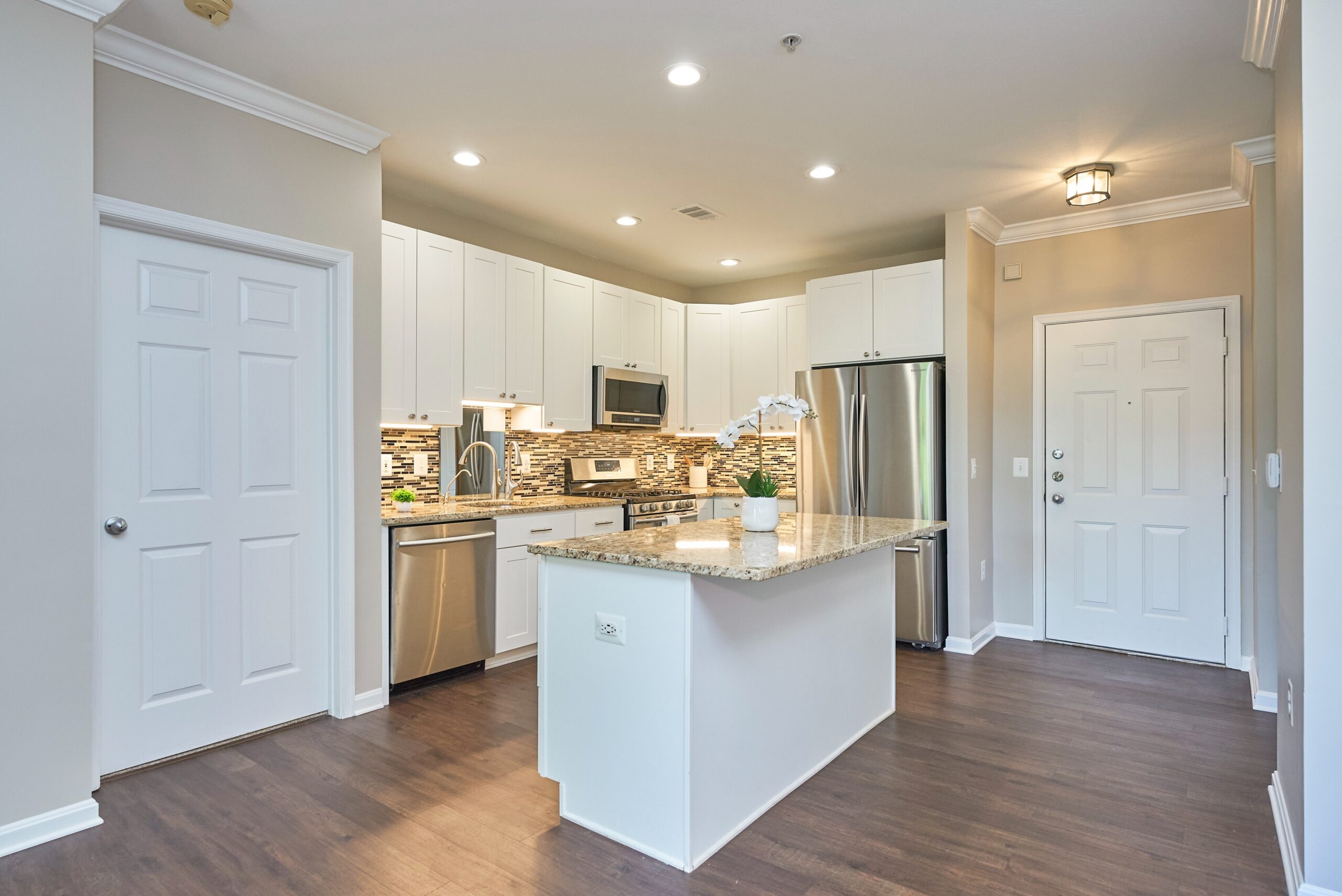 Open kitchen in luxury condo with intricate backsplash, stainless steel appliances, and a large island