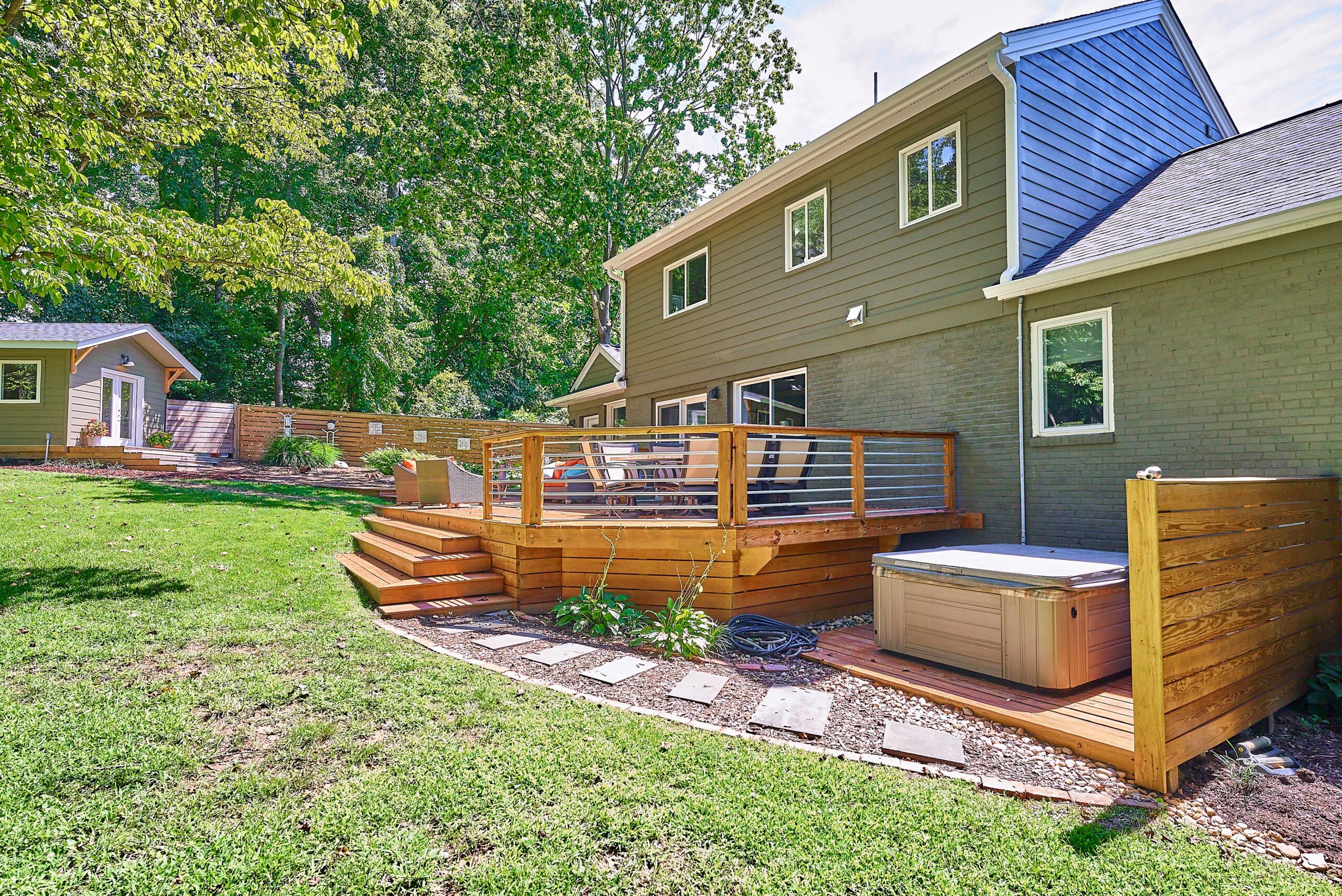 Professional photo of rear exterior of custom home in Falls Church, Virginia. Shows hot tub and flagstone path to the large deck with she-shed in the background.