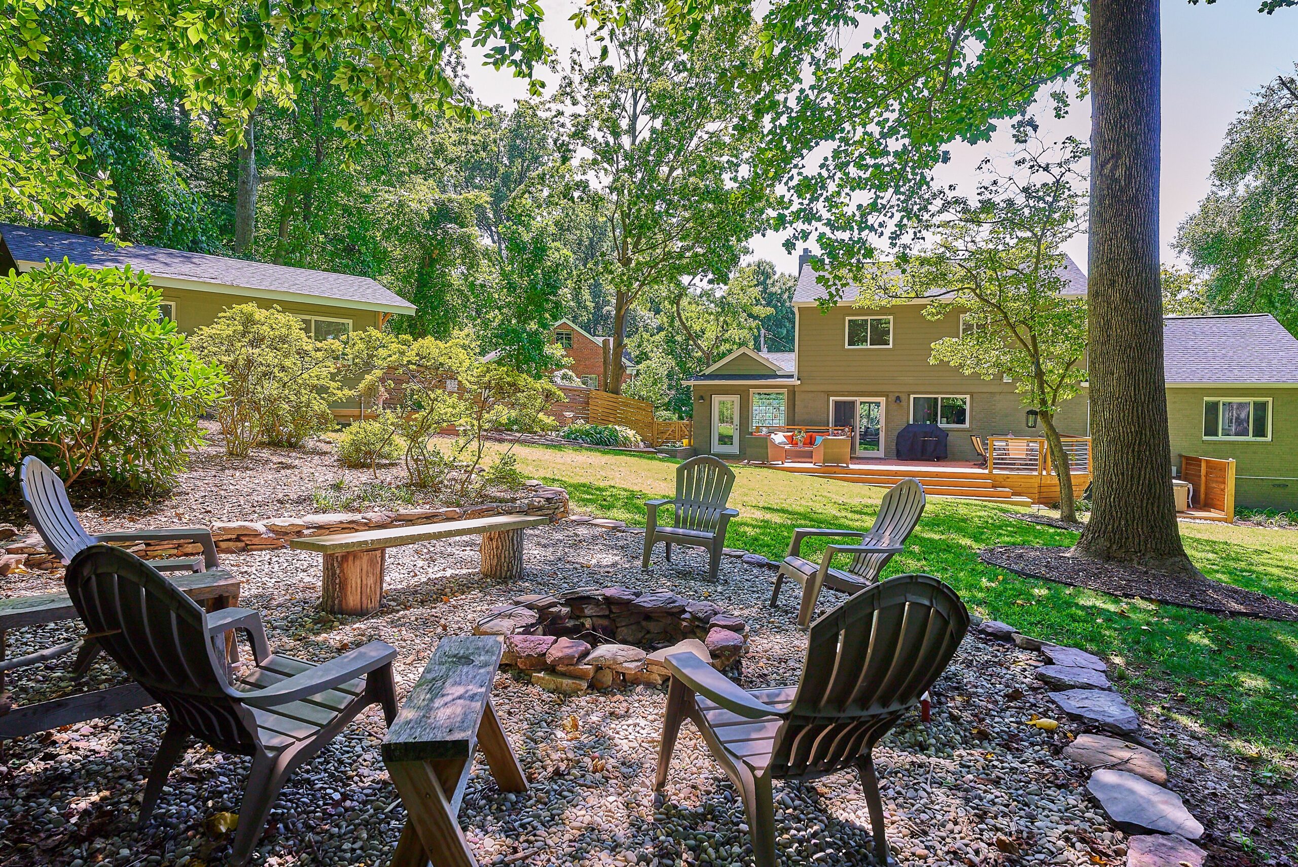 Professional photo of rear exterior of custom home in Falls Church, Virginia. Shows fire pit with several chairs in the foreground and grassy flat space in the background near the home.
