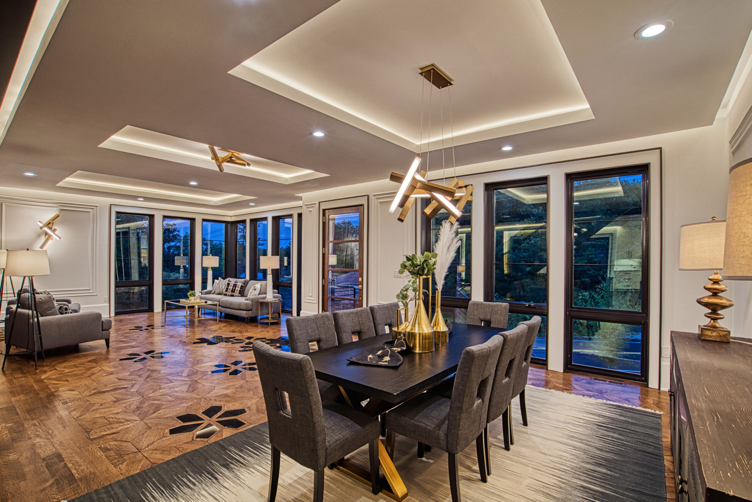 dusk photo of interior of new construction luxury home with open floor plan, dining area in the foreground and sitting area in background, tray ceilings