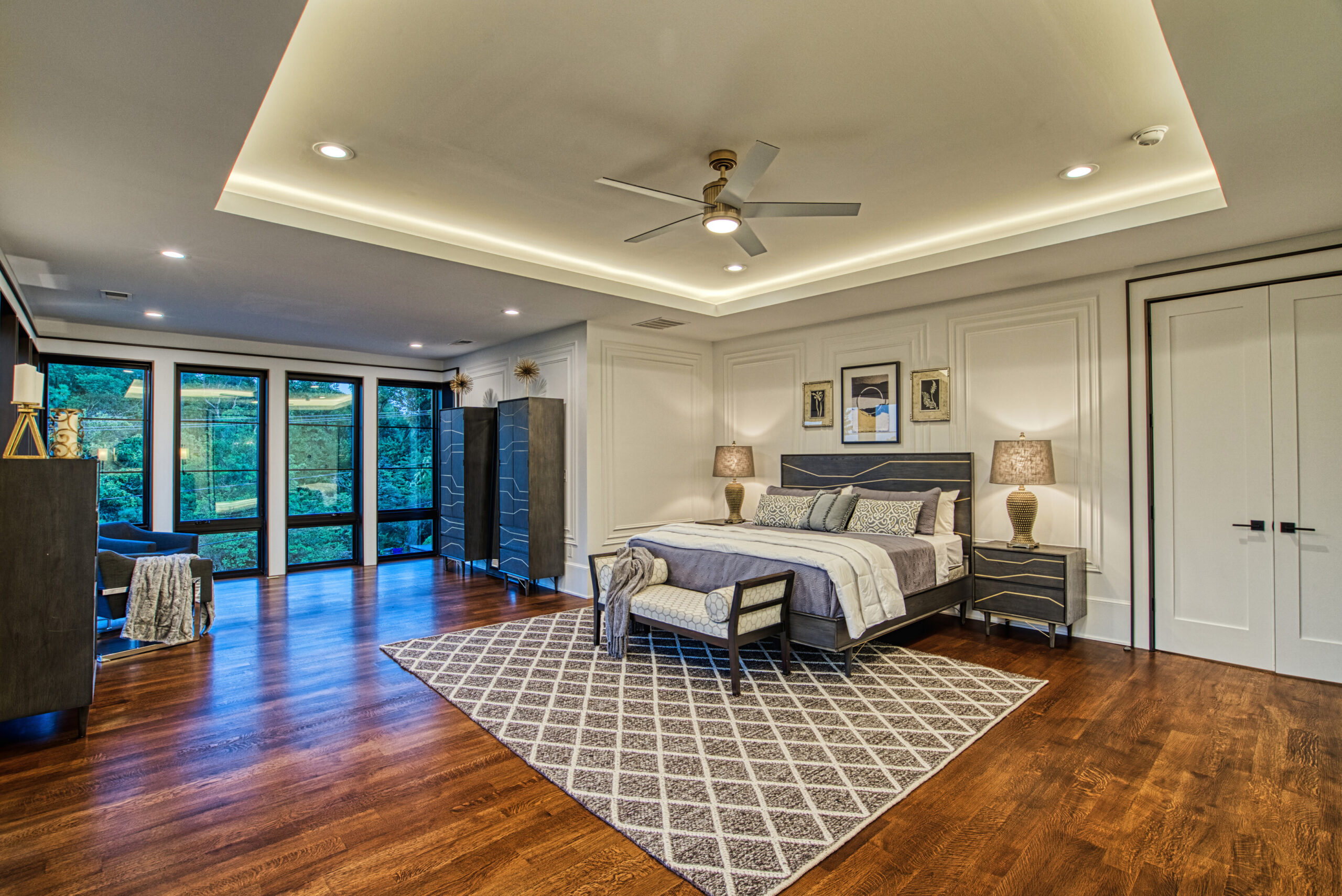 Master bedroom in modern luxury new construction home with huge tray ceiling, custom hardwood floors, and floor to ceiling windows.