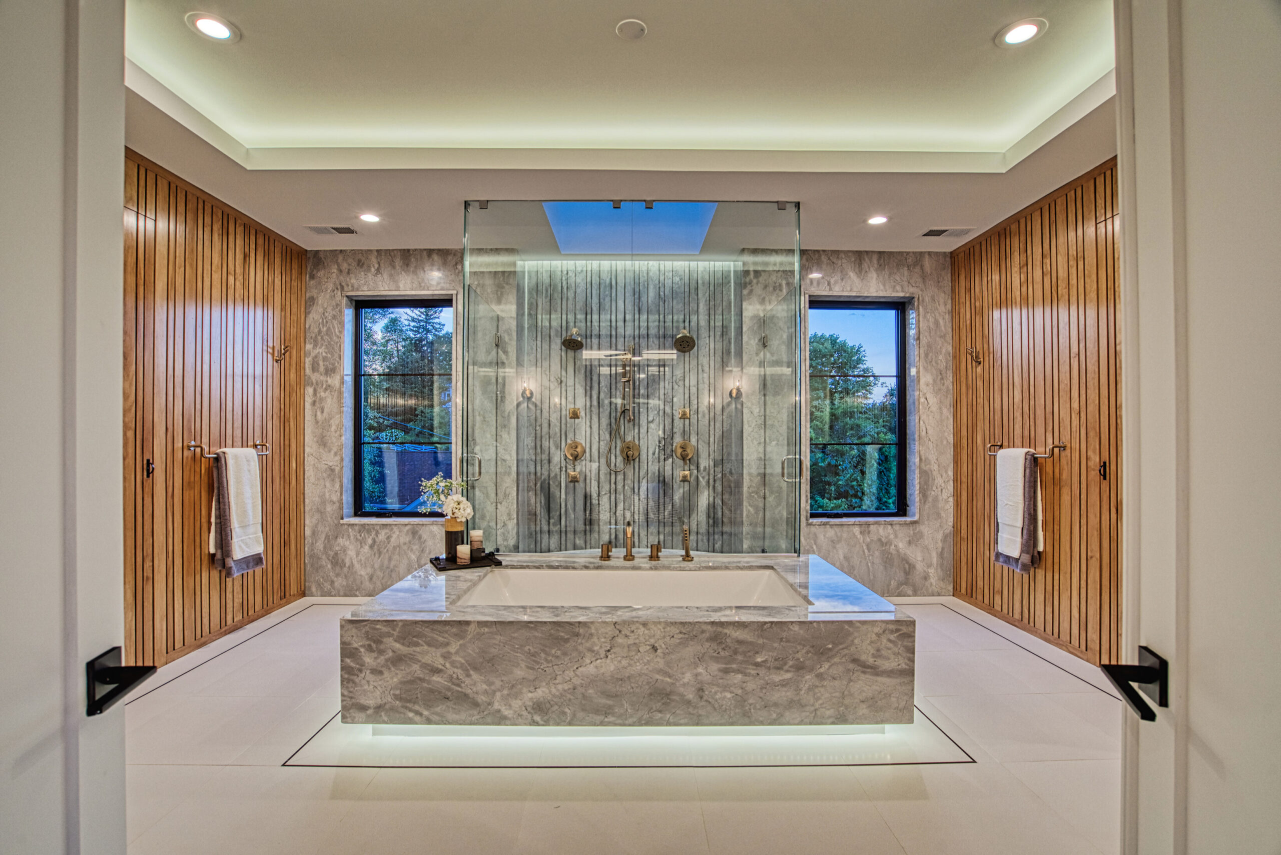 head on view of Bathroom in luxury new construction home with large marble jacuzzi tub and glass enclosed shower behind, wood paneled storage on either side. 