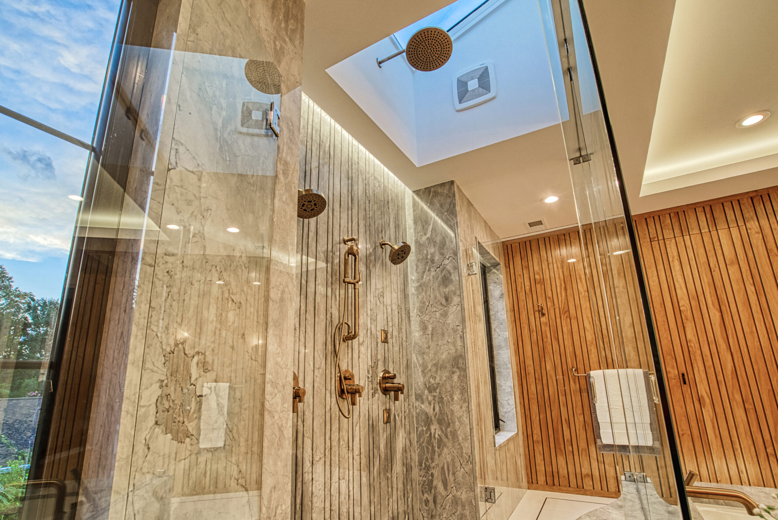 stunning marble, glass-enclosed shower with gold fixtures, rain head in recessed ceiling with skylight