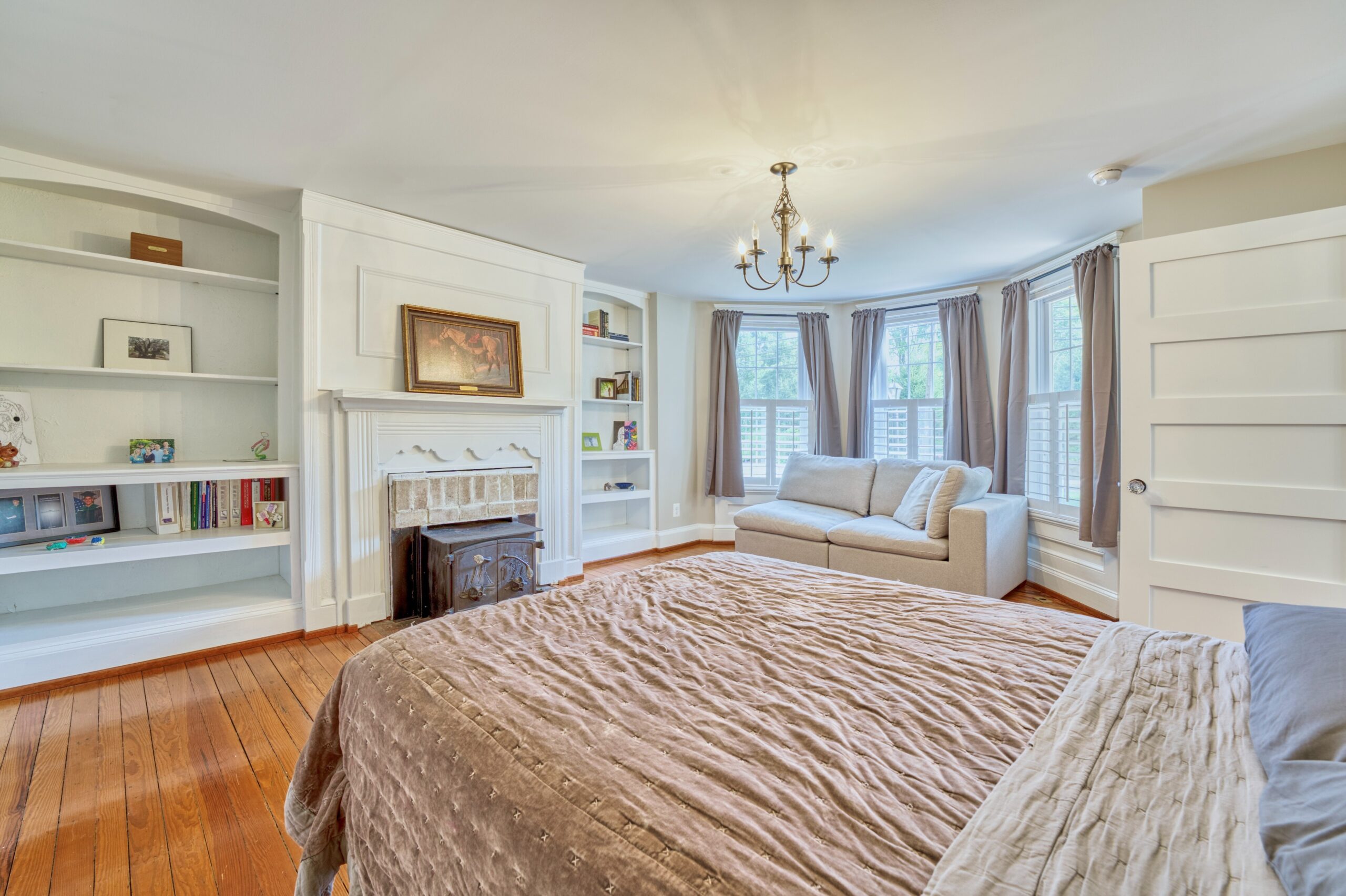 dramatic large bedroom in historic home in Hamilton, VA with built-in bookshelves on either side of a fireplace, chandelier and lounge chair in window nook. 
