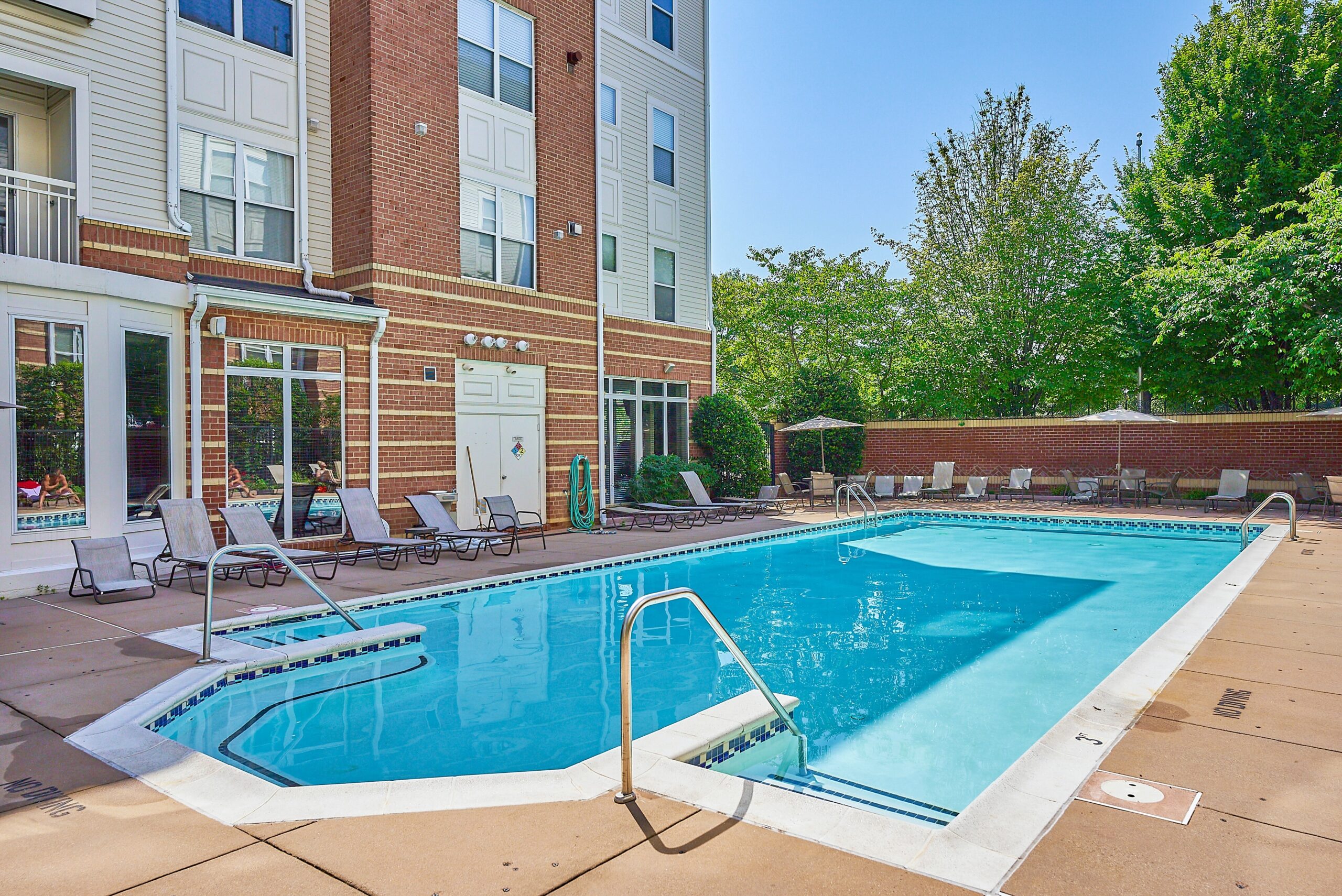 Large outdoor condo pool with sun and lounge chairs around it on a sunny day