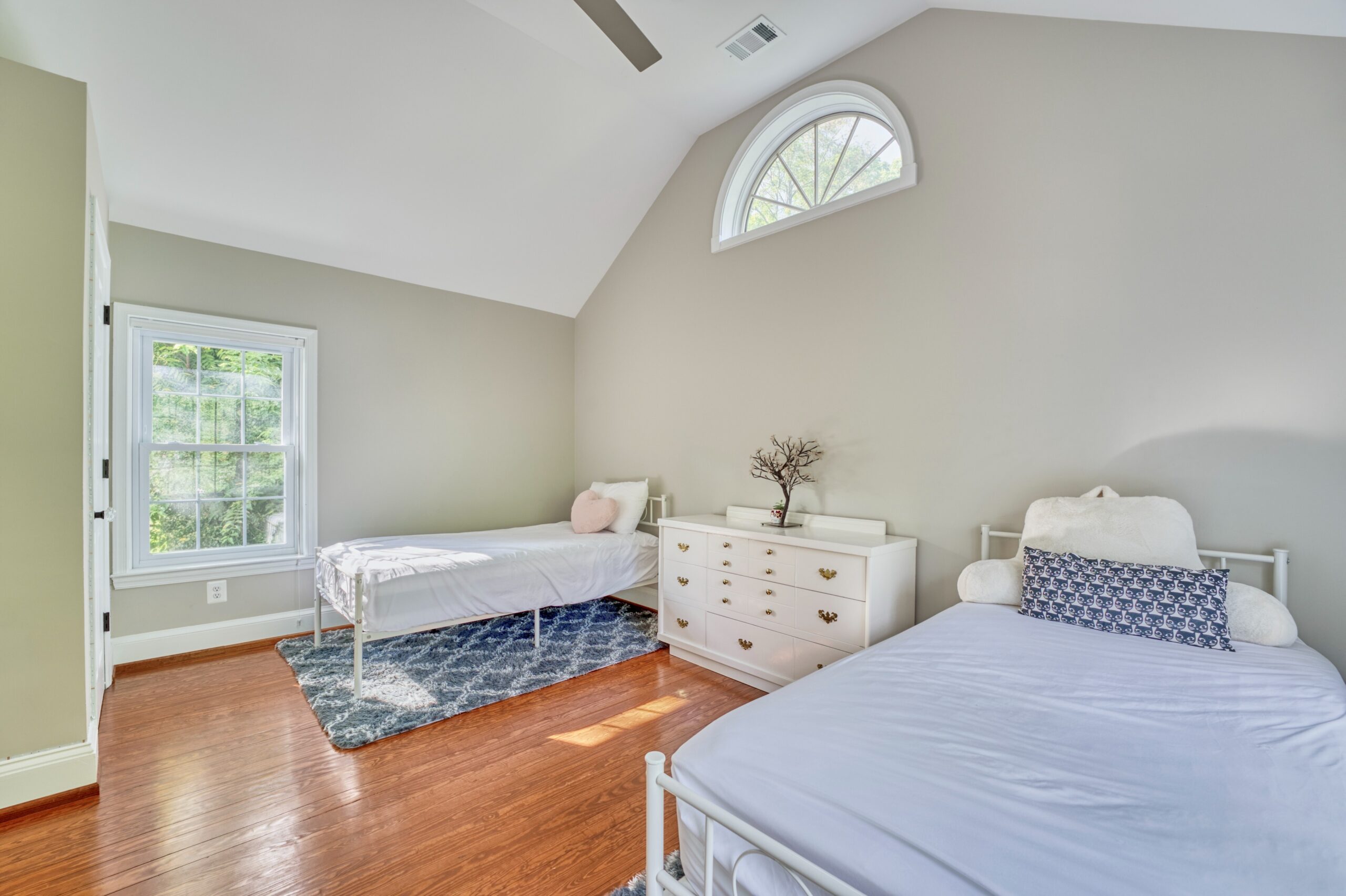Large bedroom with vaulted ceiling and half circle window centered near the ceiling, in historic home staged with 2 twin beds 