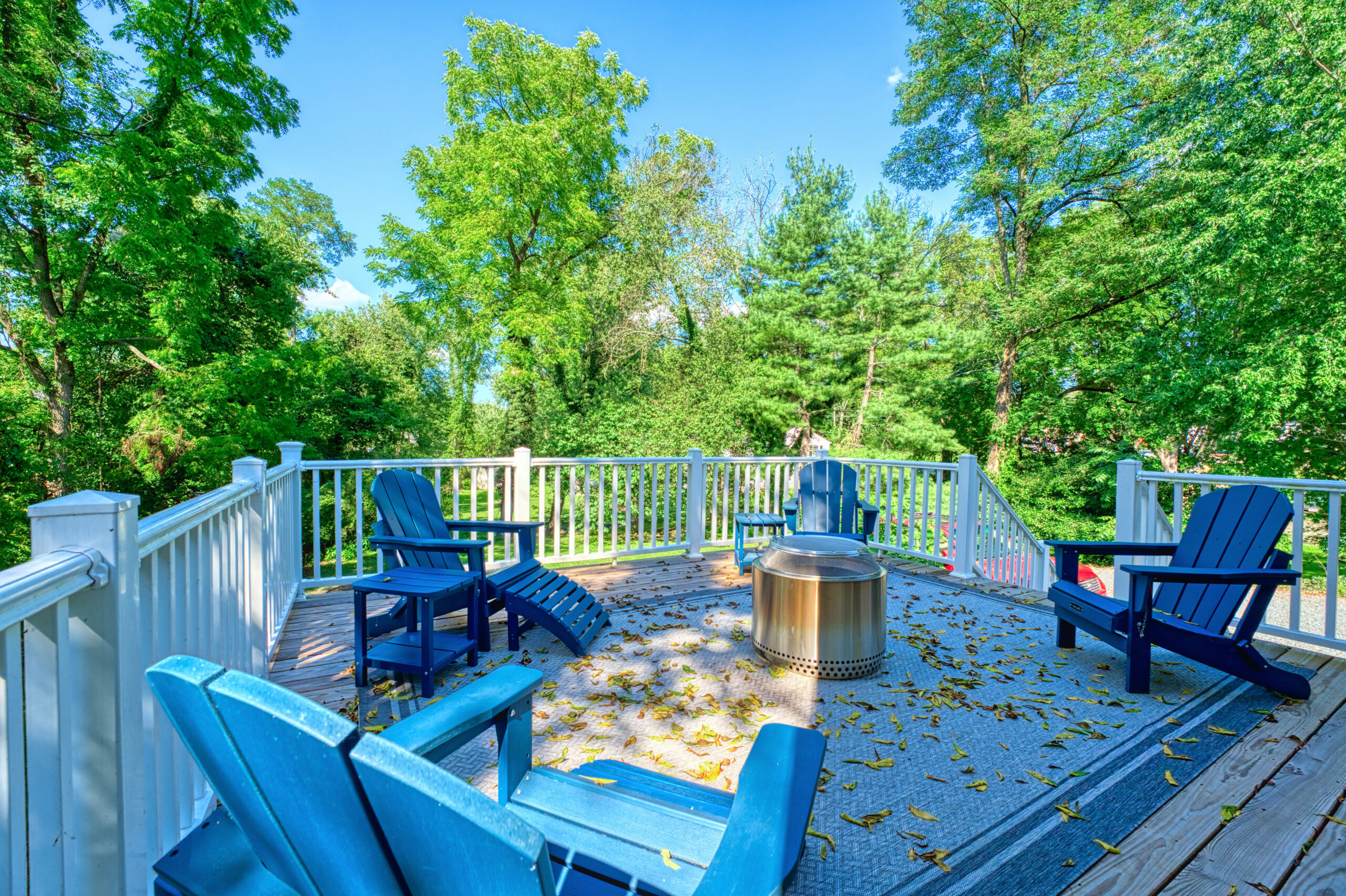 large back deck off historic home in Hamilton, VA on a bright sunny day with lush trees surrounding the background. Adirondack chairs centered around a portable fire pit.