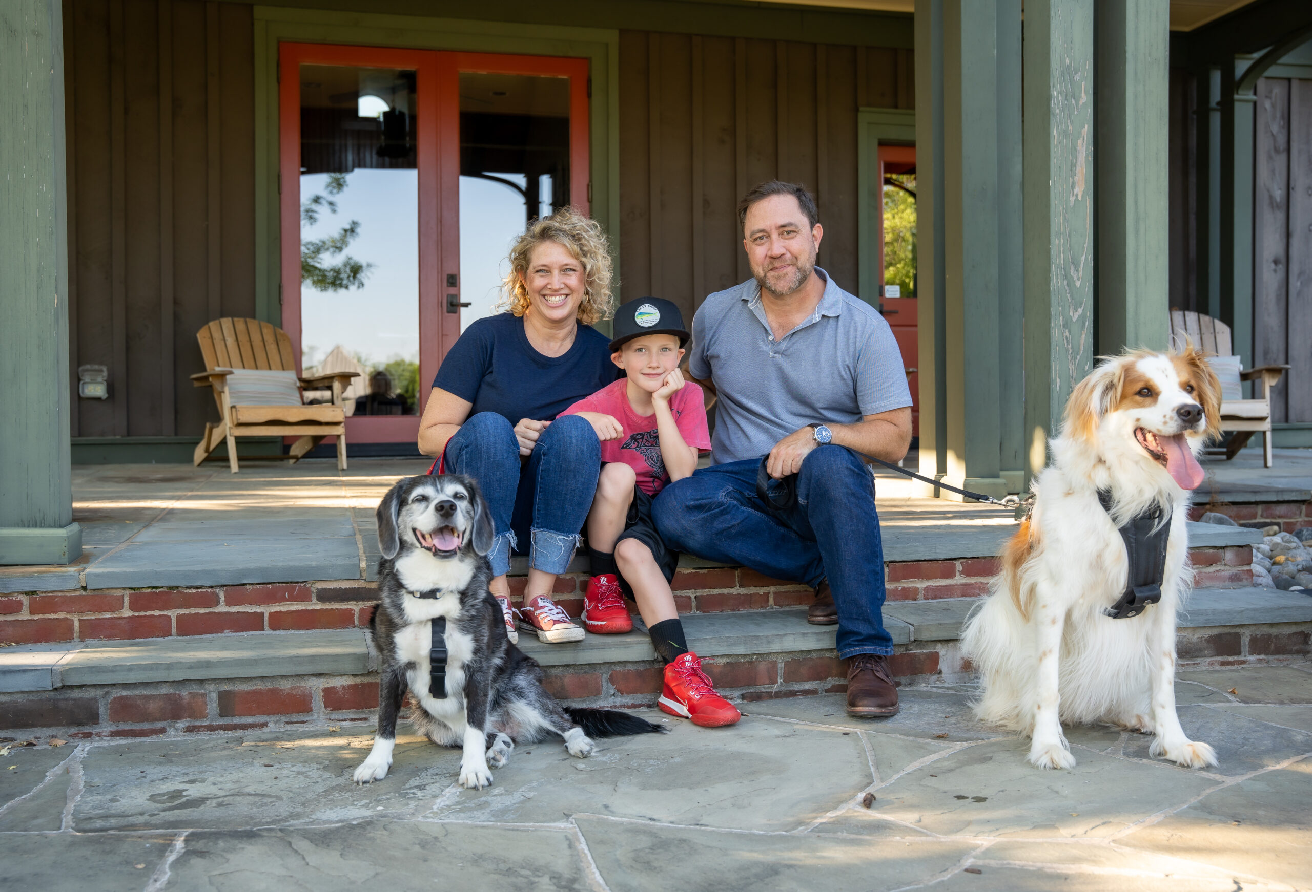 personal branding photo for realtors showing a mother and father, both realtors, and young son with their 2 dogs on steps outside a community center