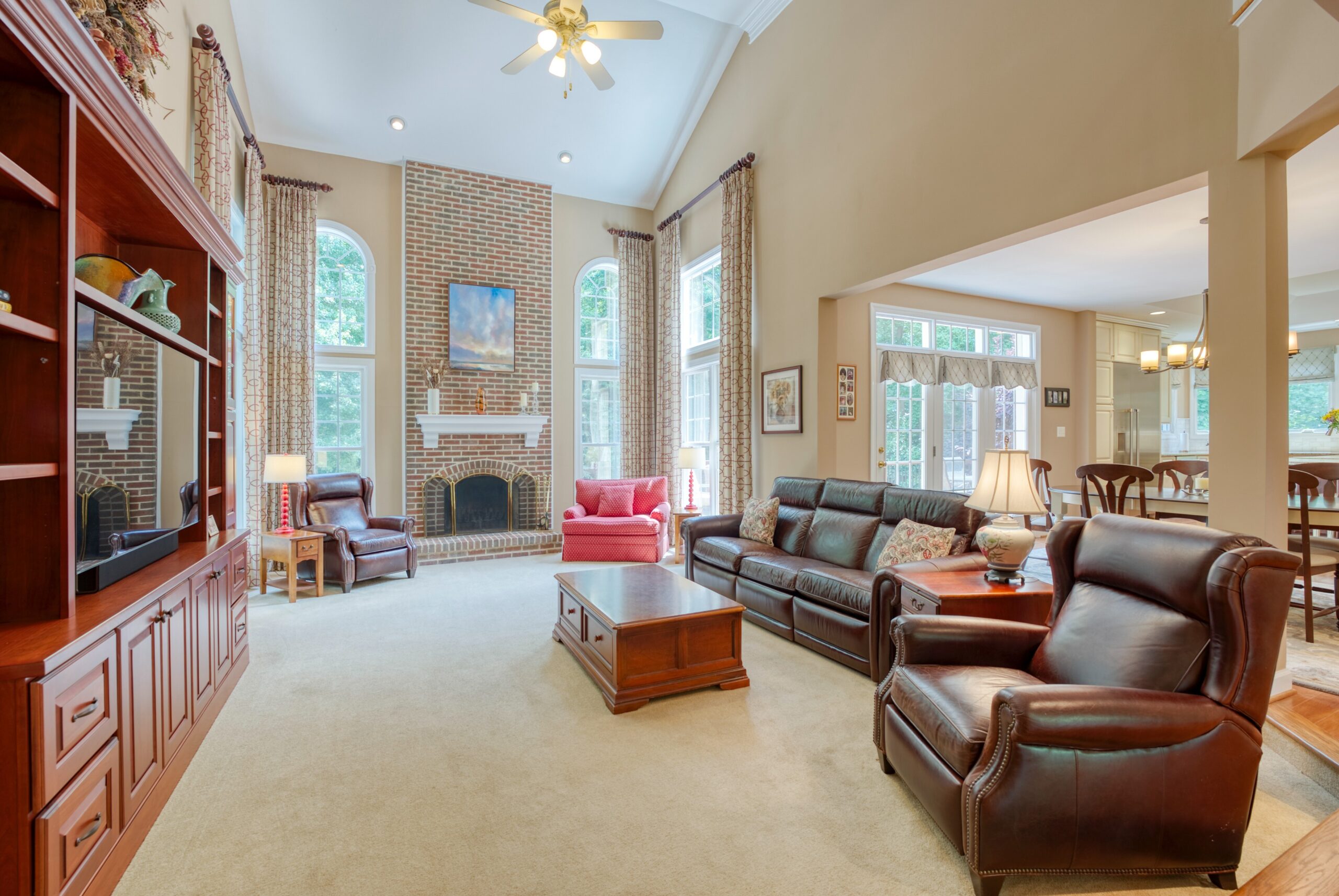 Living room of stately home in Fairfax, VA - showing2-story brick fireplace with floor-to-ceiling windows on either side and open floor plan glimpsing the kitchen. 10703 Ox Croft Ct, Fairfax Station, VA