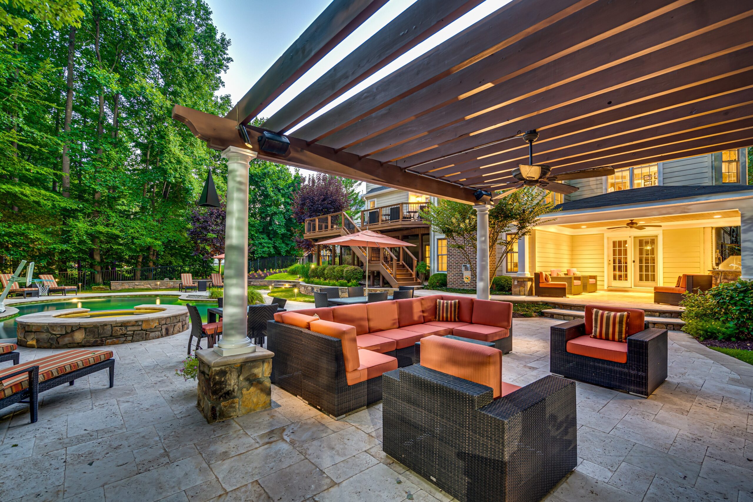 Exterior lounge area at dusk by the pool with the warmly lit home and deck in the background. 10703 Ox Croft Ct, Fairfax Station, VA