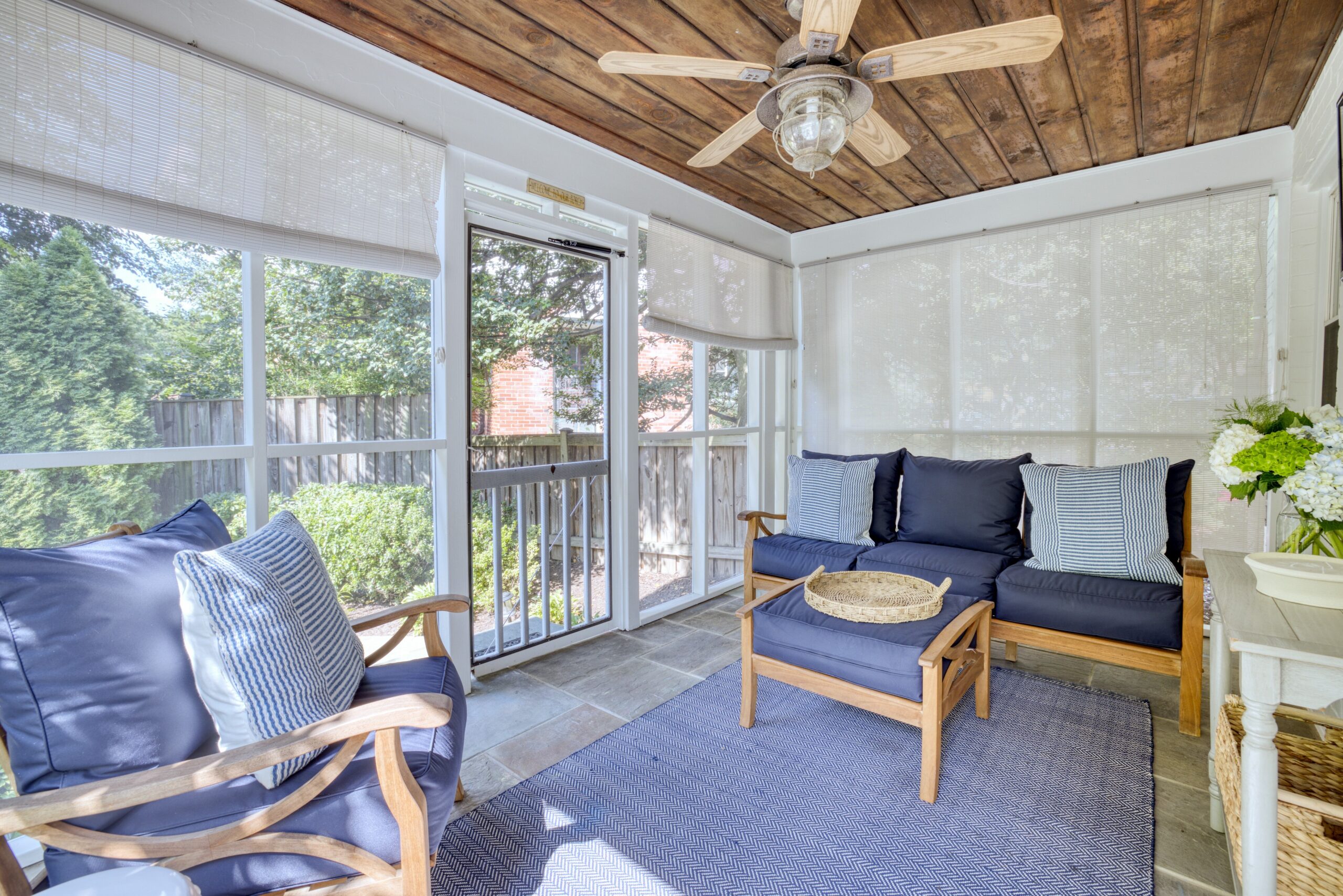 Interior professional photo of screened in porch of 1946 Cape Cod home in Alexandria, VA with blues and wooden patio furniture and ceiling fan