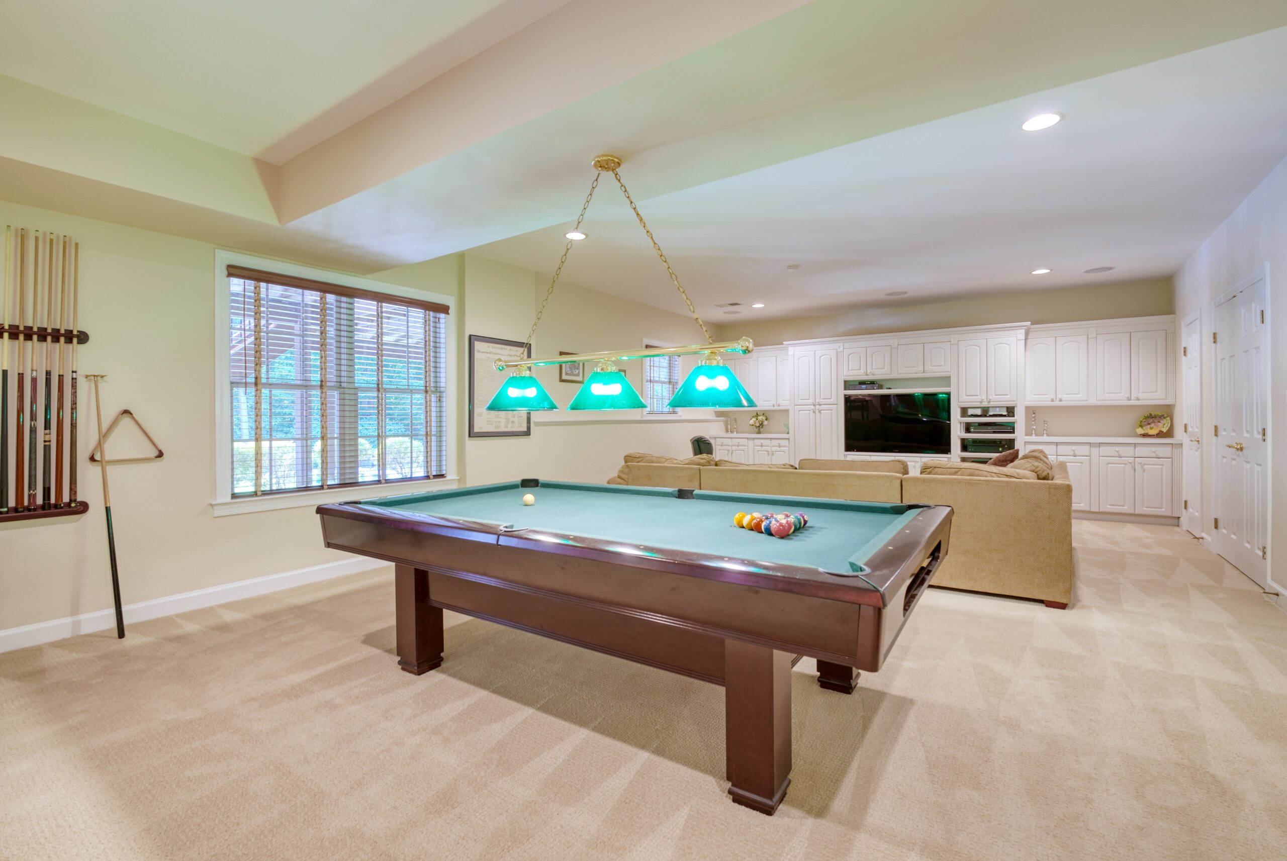 Finished basement with billiards table in the foreground and living TV area in the background, with built-in white cabinets around the TV. 10703 Ox Croft Ct, Fairfax Station, VA