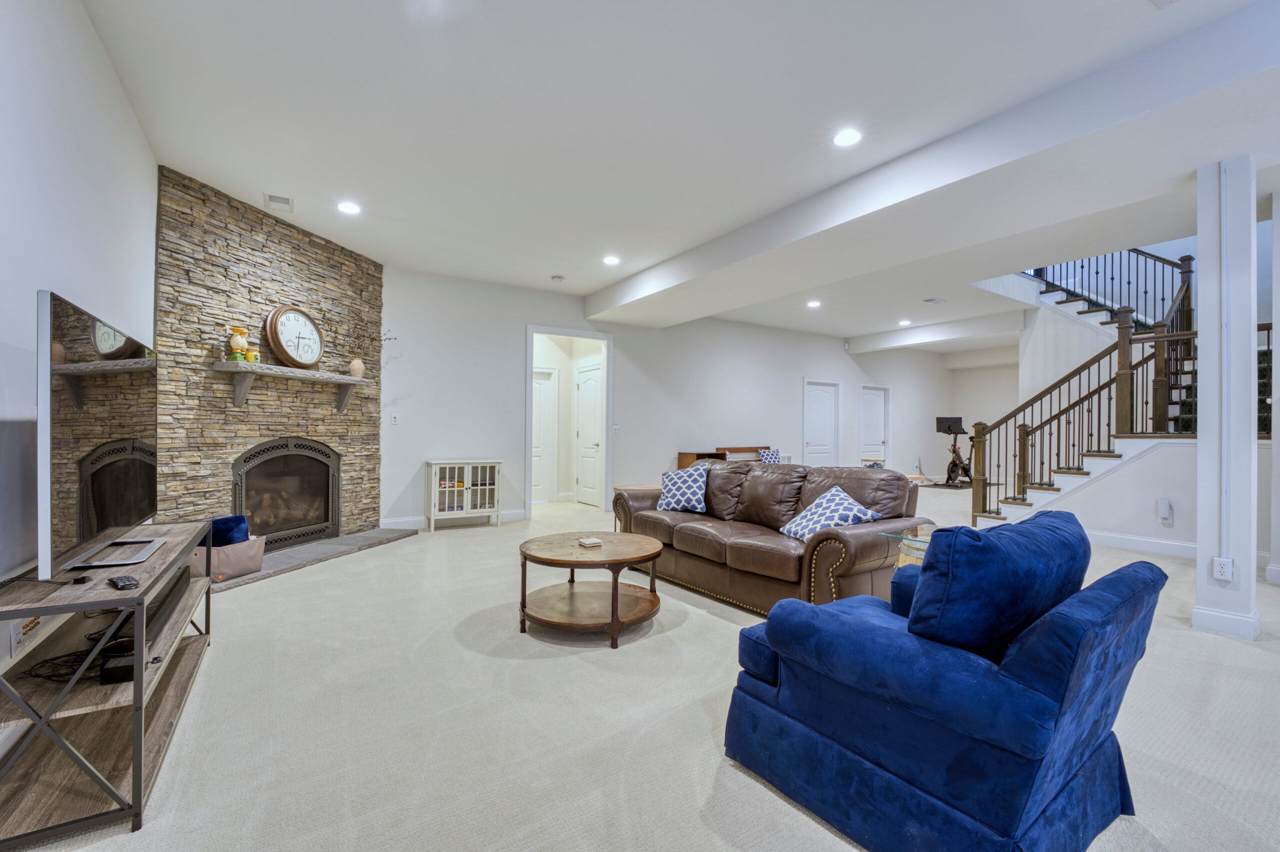 23734 Heather Mews Dr, Ashburn - professional interior photo showing large open finished basement space, stone floor-to-ceiling fireplace situated in an angled corner