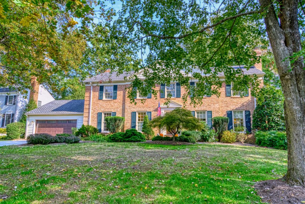 Professional exterior photo of 8305 River Falls Dr, Potomac, MD - front shot. All brick home with attached 2-car garage. Large tree in the front hard obscures part of the home.