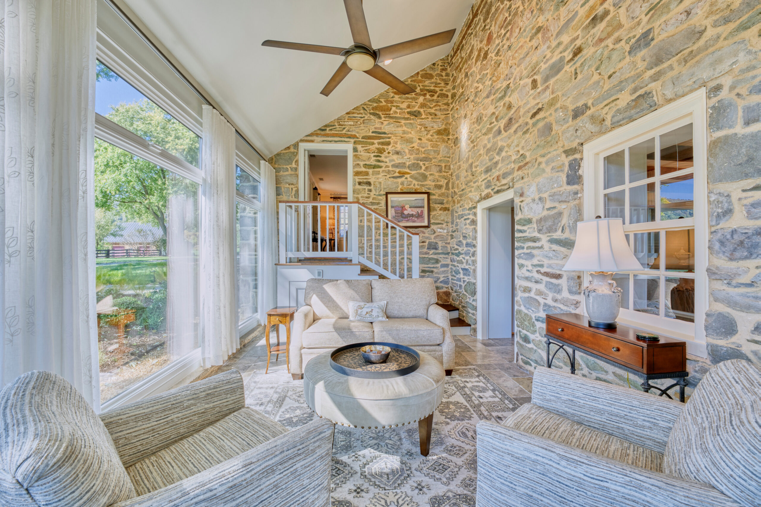 Professional interior photo of main house of Historic Hearthstone Manor: 35428 Appalachian Trail Rd, Round Hill, Virginia - showing brightly lit sunroom with wall to wall windows on the left and stone walls on the right and straight ahead