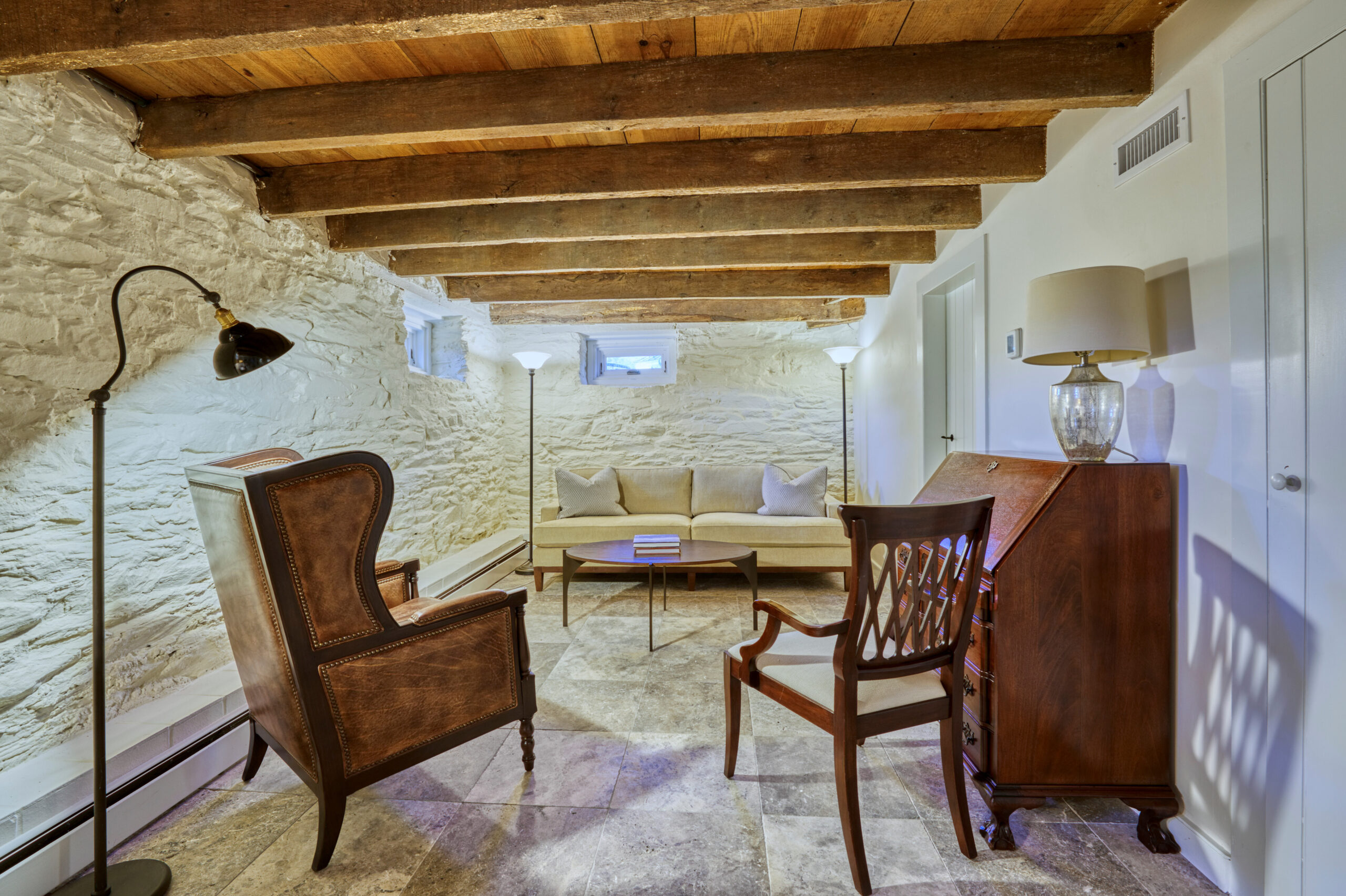 Professional interior photo of main house of Historic Hearthstone Manor: 35428 Appalachian Trail Rd, Round Hill, Virginia - showing basement sitting room with painted stone walls, and exposed wooden ceiling beams