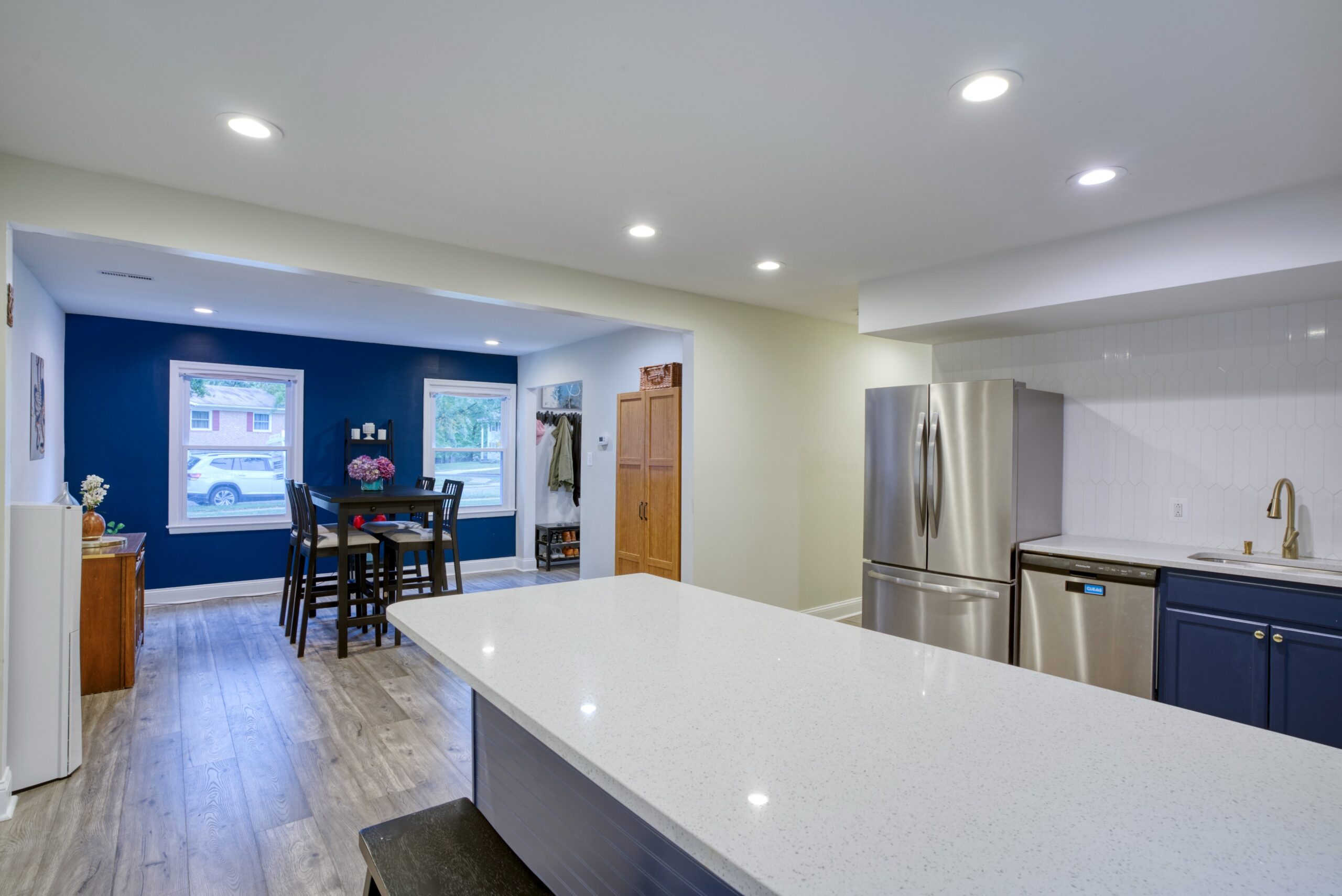 Interior professional photo of 9015 Longbow Rd - showing newly remodeled and upgraded kitchen with stainless appliances, huge quartz peninsula for dining, and navy contrast colors. Glimpse of dining area in background
