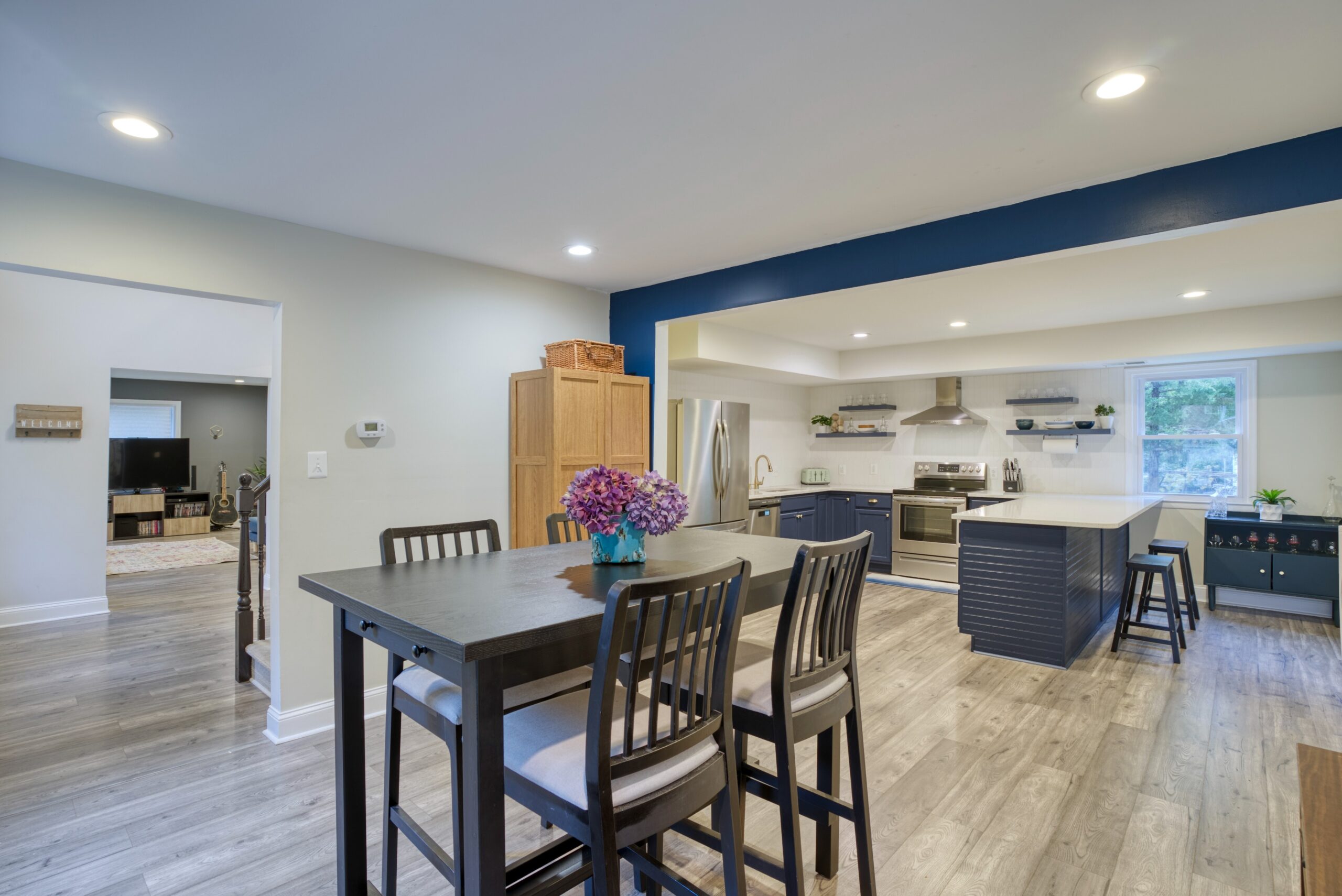 Interior professional photo of 9015 Longbow Rd - showing newly remodeled and upgraded kitchen with stainless appliances, huge quartz peninsula for dining, and navy contrast colors in the background - dining area in the foreground