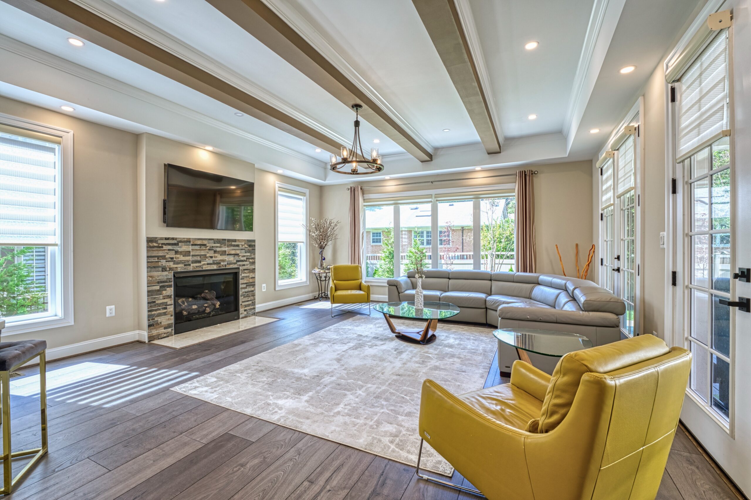 professional Fusion photo of the interior of a home in McLean, VA - showing living room with tray ceiling with exposed beams, windows on 3 sides and gas fireplace.