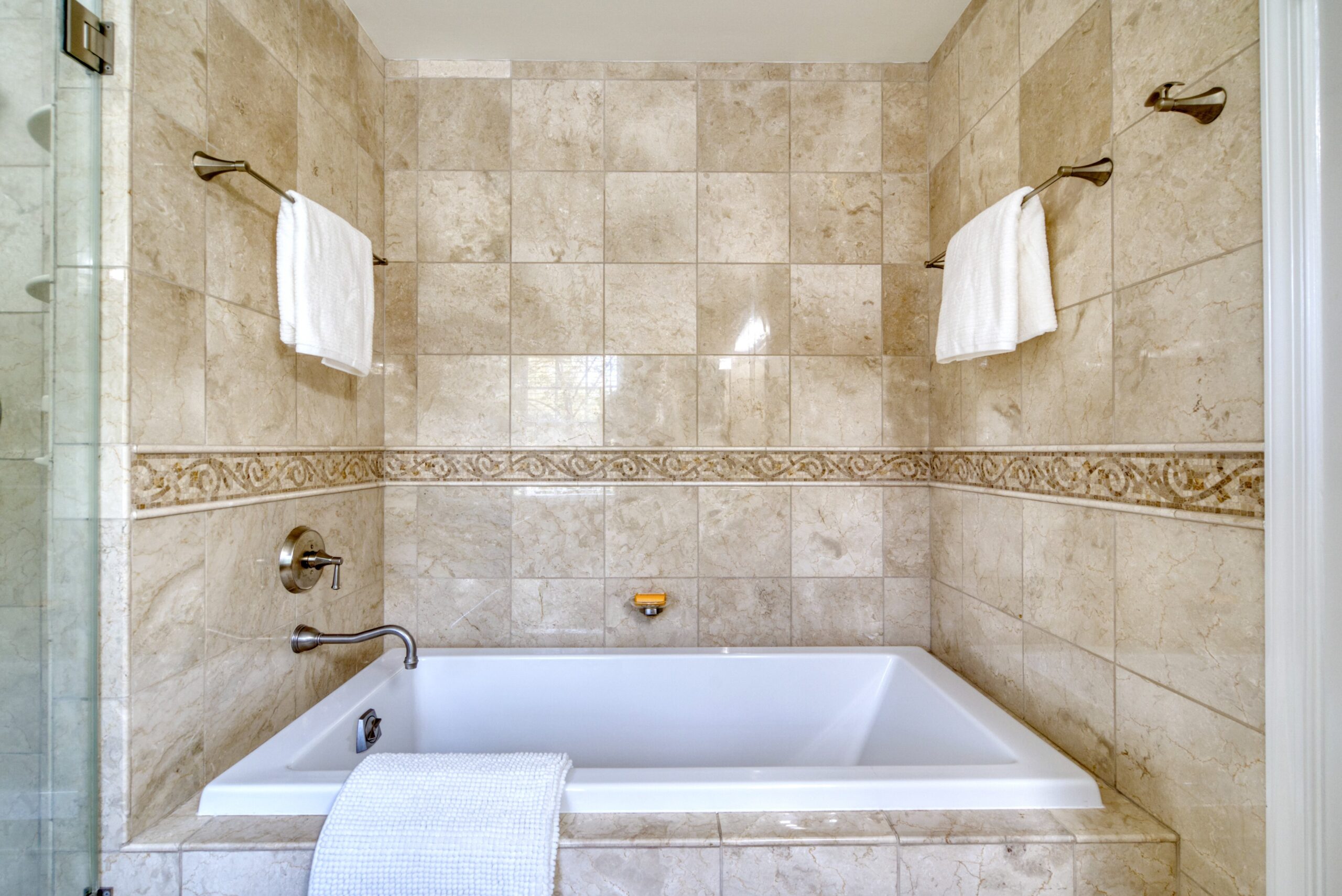 Professional interior photo of 8305 River Falls Dr, Potomac, MD - showing square soaking tub surrounded by floor to ceiling beige tile in master bathroom