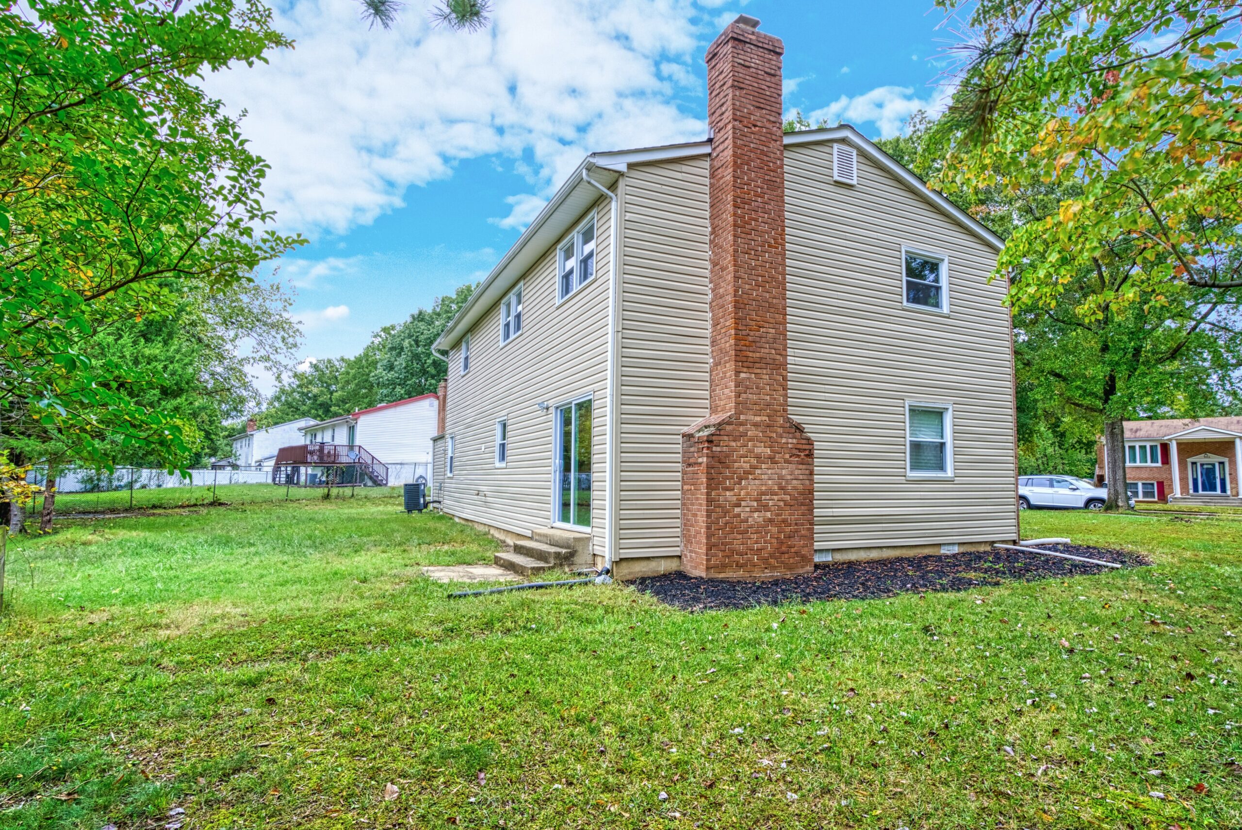 Exterior professional photo of 9015 Longbow Rd - showing the rear from the left side angle. Red brick chimney on the end, beige siding, flat front and back yard.