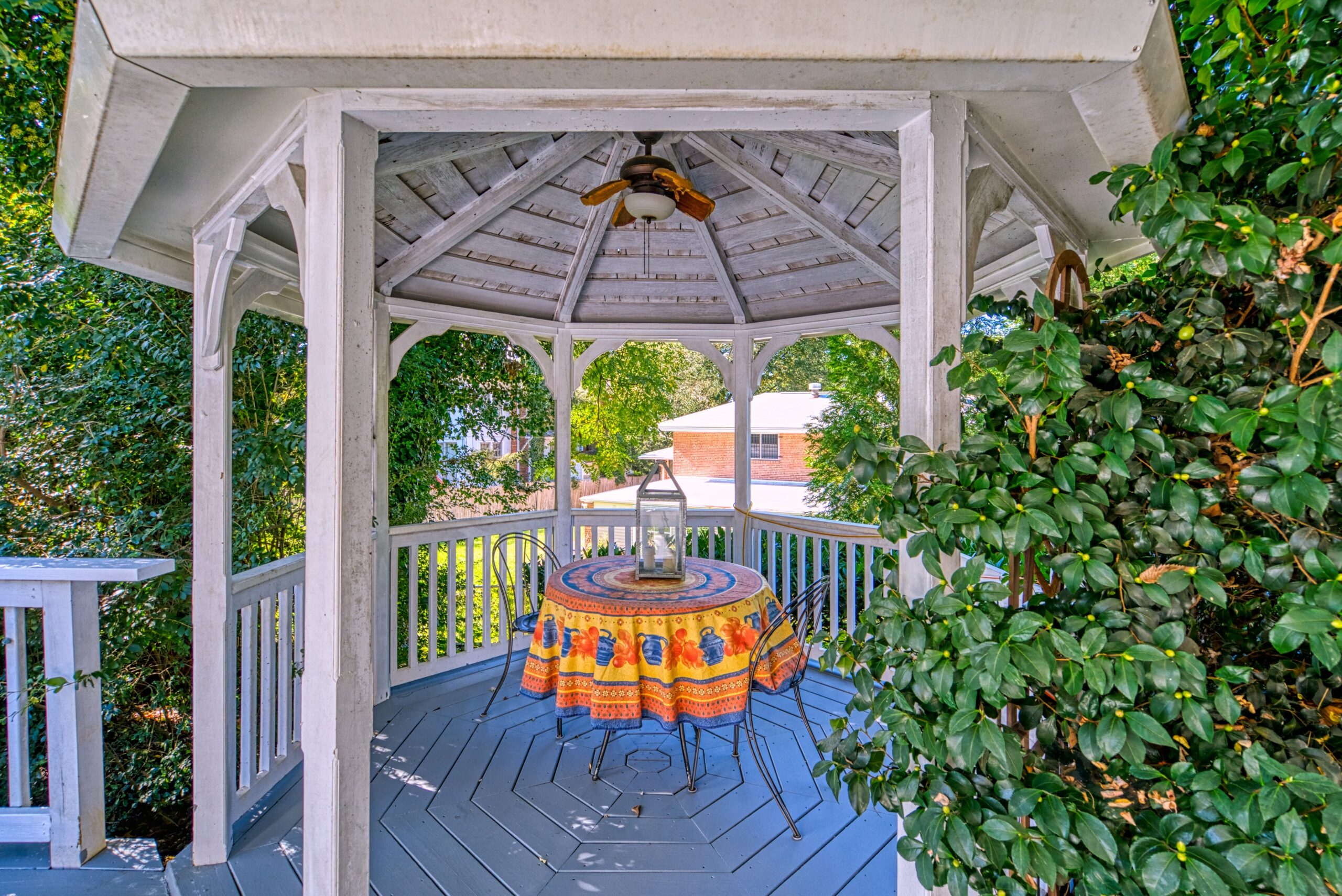 Exterior professional photo of 1826 Varnum St NW - showing a painted white wooden gazebo with a ceiling fan on a deck and cute bright tablecloth on patio set
