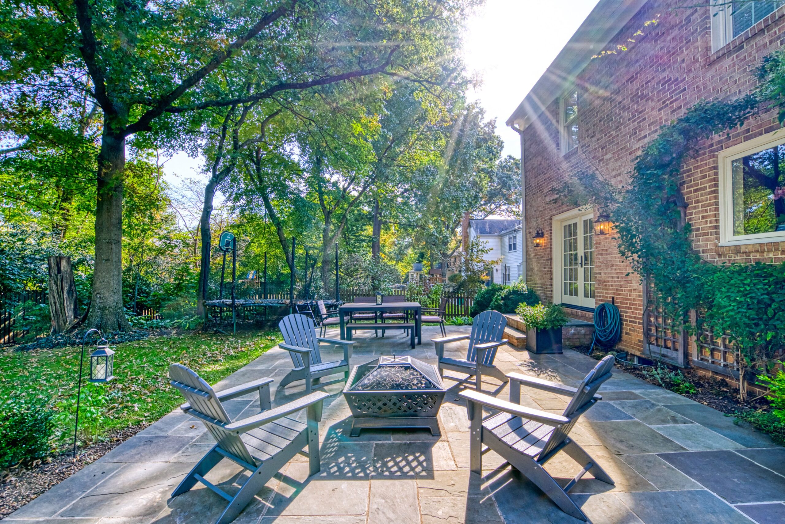 Professional exterior photo of 8305 River Falls Dr, Potomac, MD - rear patio with adirondack chairs around a fire pit with rays of sunshine