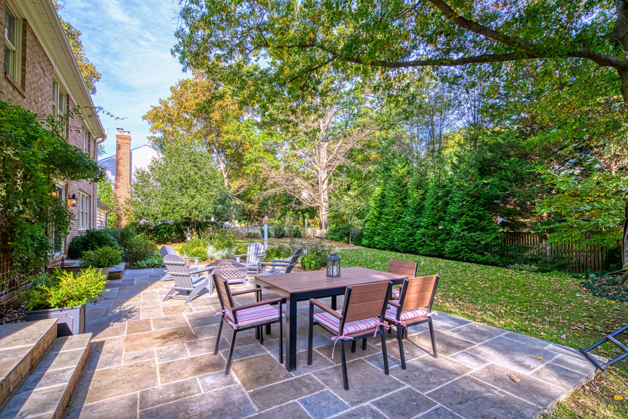 Professional exterior photo of 8305 River Falls Dr, Potomac, MD - rear shot showing most of large patio with 2 sets of patio furniture behind the red brick home, and the flat backyard