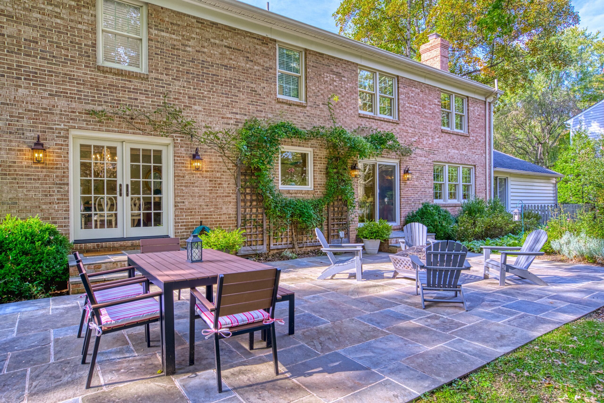 Professional exterior photo of 8305 River Falls Dr, Potomac, MD - rear shot showing most of large patio with 2 sets of patio furniture behind the red brick home