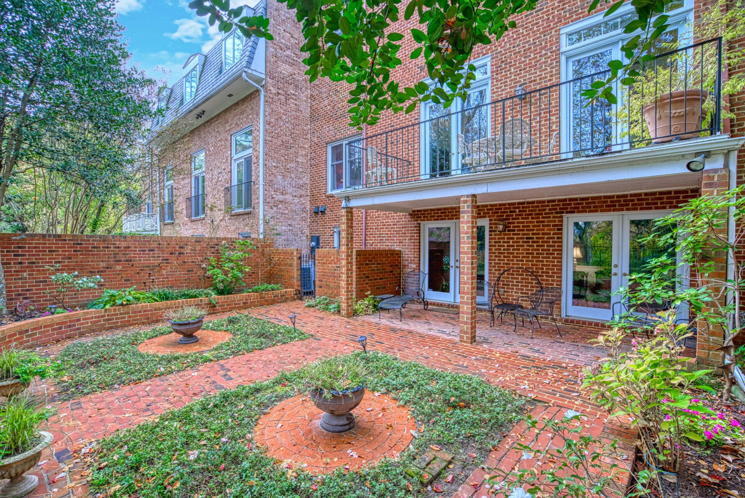 Exterior professional photo of 1324 Skipwith Road - showing rear exterior from the right angle. Brick paths with 2 landscaped ivy patches, covered brick patio and balcony