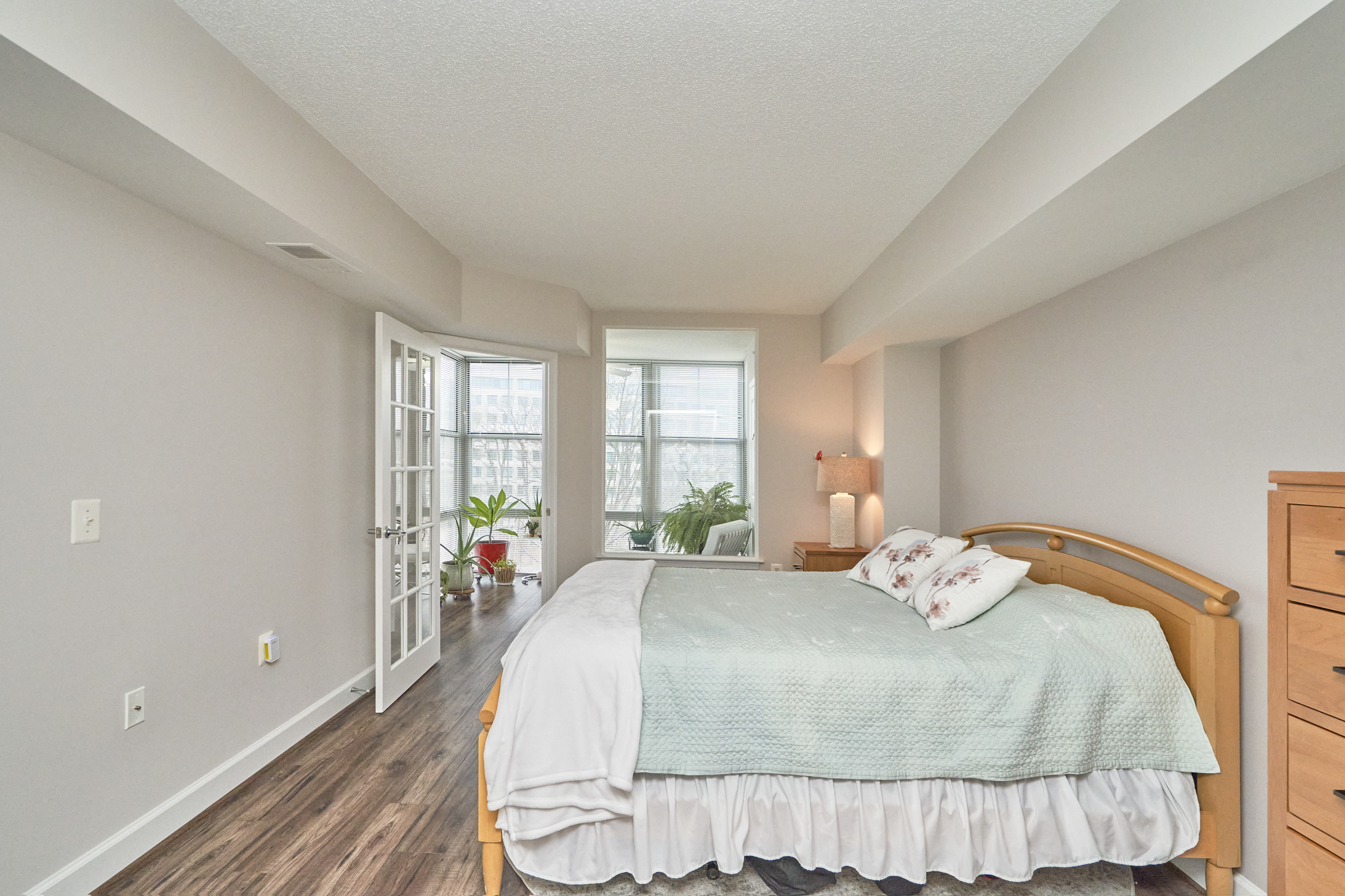 Interior professional photo of 11800 Sunset Hills Road Unit #811, showing one of the bedrooms with recessed ceiling, bed in the foreground, and view of the connected sunroom in the background