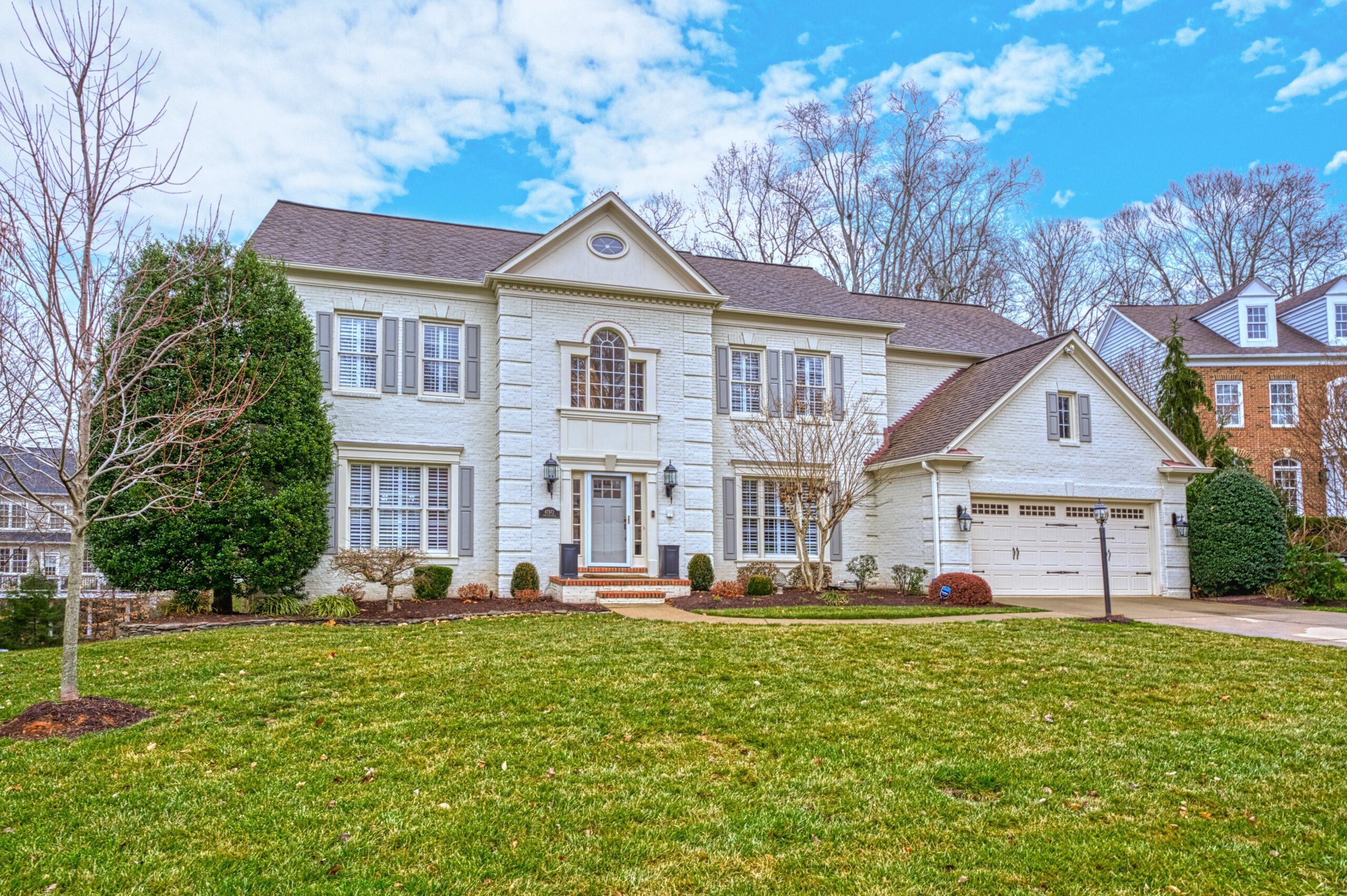 Exterior professional photo of 47572 Compton Circle, Sterling, VA - showing the front which is white stone with a 2 car garage and brick path