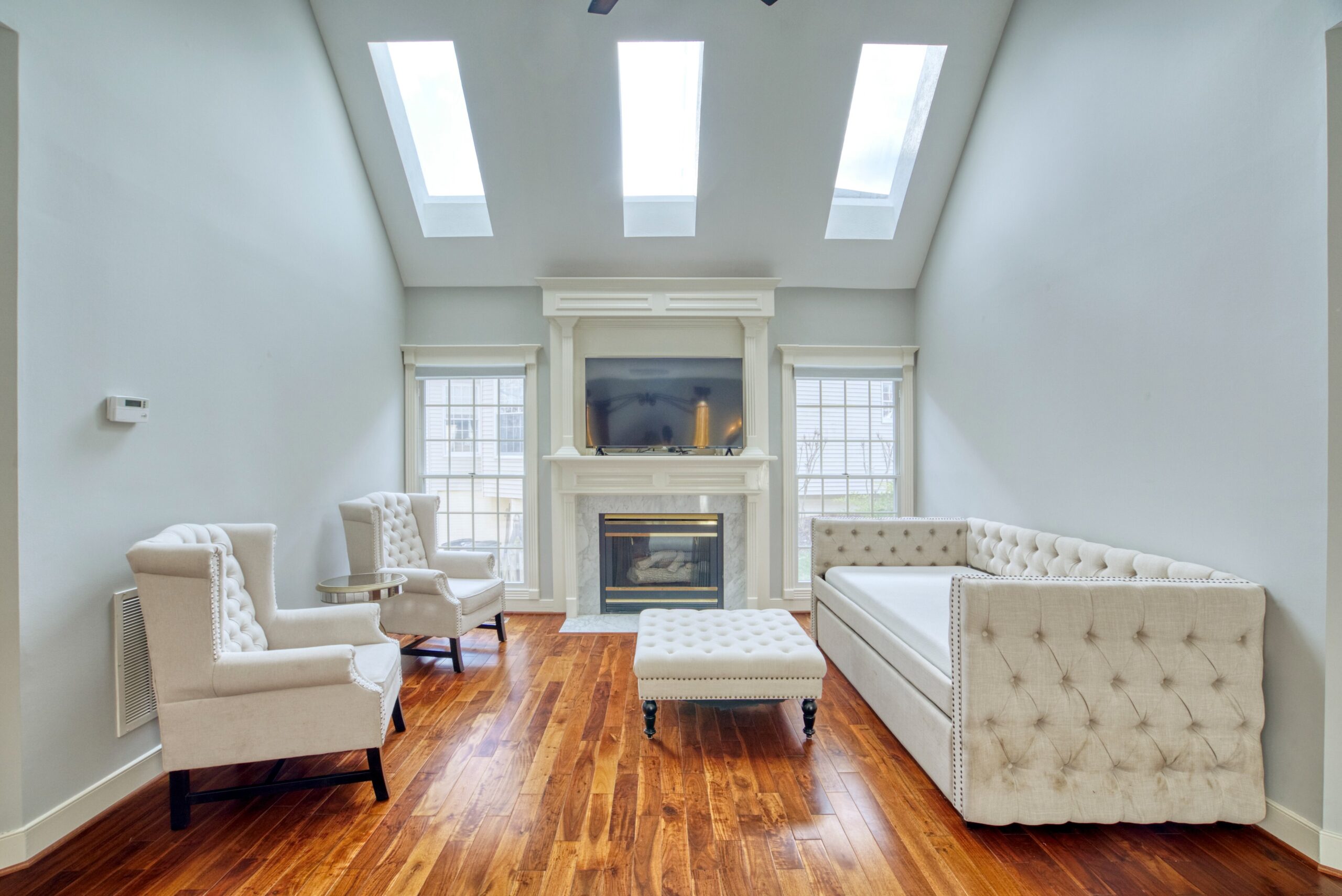 Interior professional photo of 21024 Starflower Way in Ashburn, VA - showing the sitting area in the main floor primary bedroom with vaulted ceiling, skylights, and fireplace