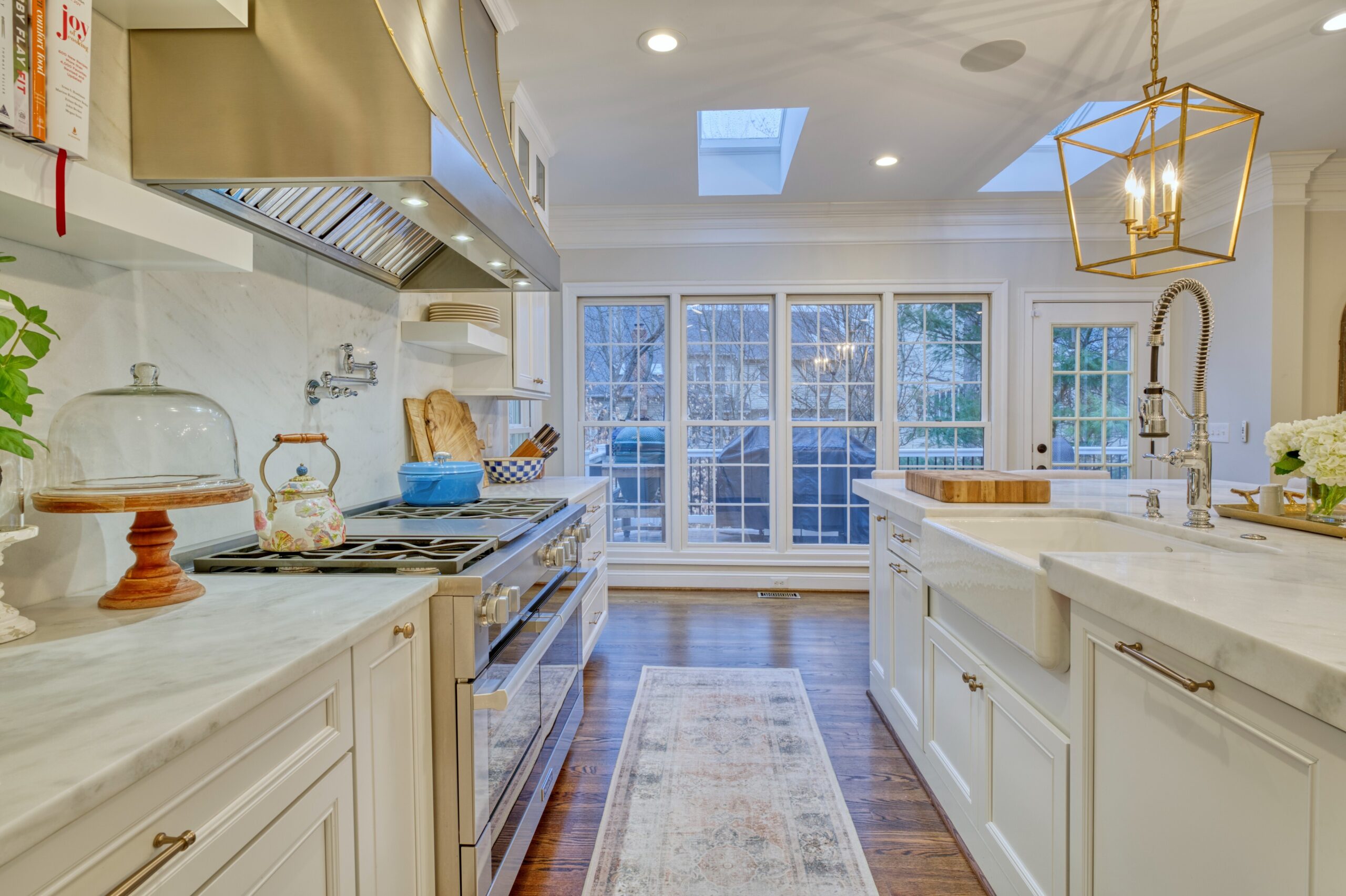 Professional interior photo of 47572 Compton Circle, Sterling, VA - showing the aisle between the stove on the left and large island on the right - white quartz countertops and brushed gold range hood and light fixtures