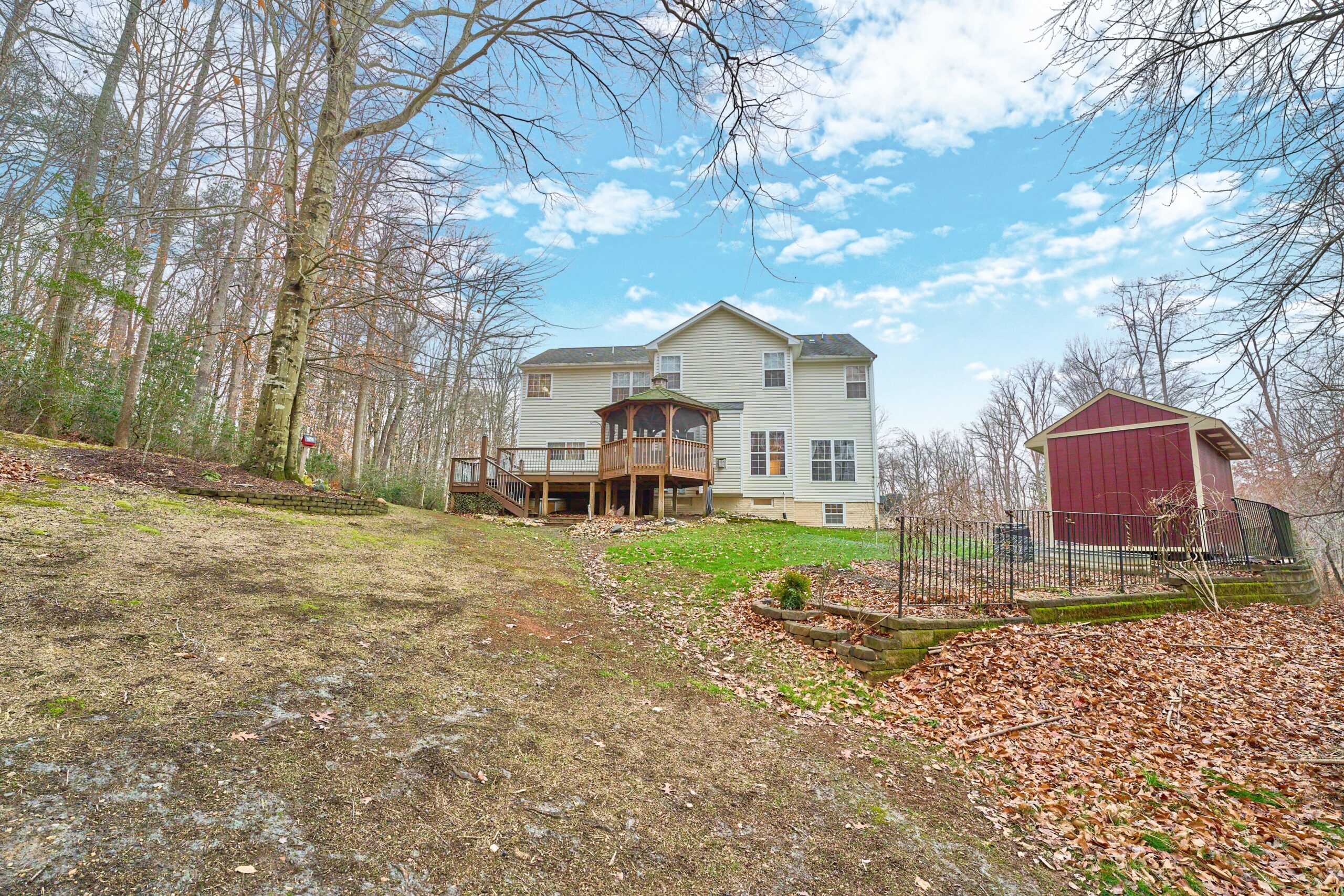 Professional exterior photo of 80 Brentsmill Drive in Stafford, Virginia - showing the rear of the home looking up from down a hill. Can see red shed in foreground and rear deck and gazebo