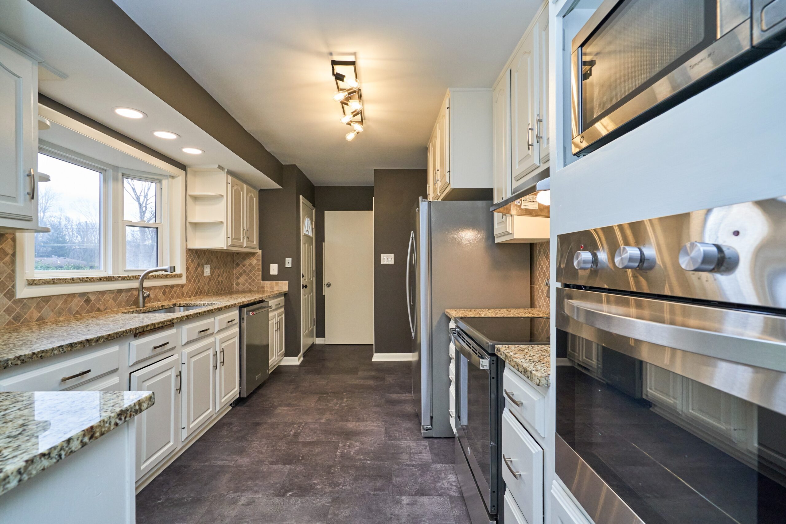 Professional interior photo of 3482 Mildred Drive in Falls Church virginia, showing the kitchen from one end with updated light fixtures, granite counters and new stainless appliances