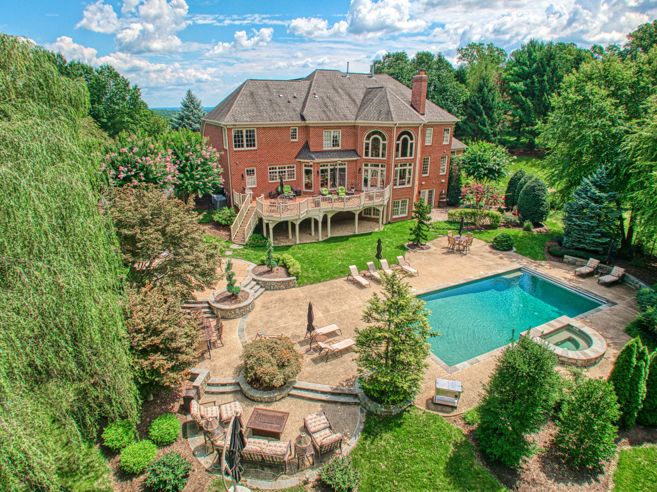 Professional exterior photo of 17087 Bold Venture Drive, Leesburg - drone photo showing the rear of the home with large deck, several stone patios and pool and hot tub