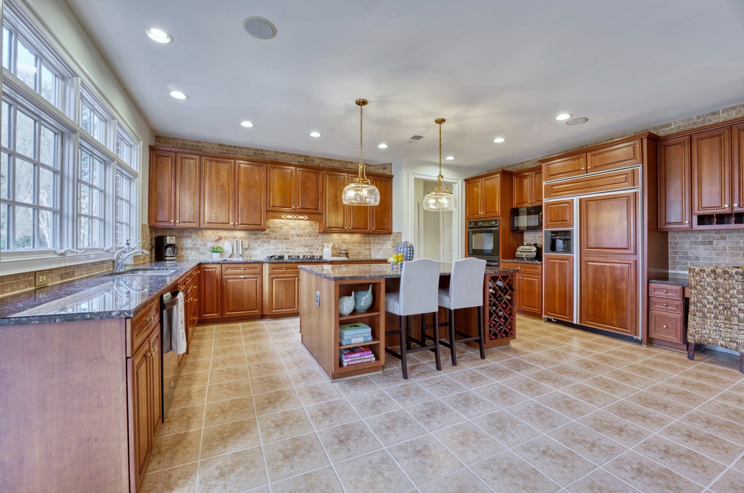Professional interior photo of 17087 Bold Venture Drive, Leesburg - showing the kitchen with walnut cabinets and custom built in fridge, large island, and tile floors.