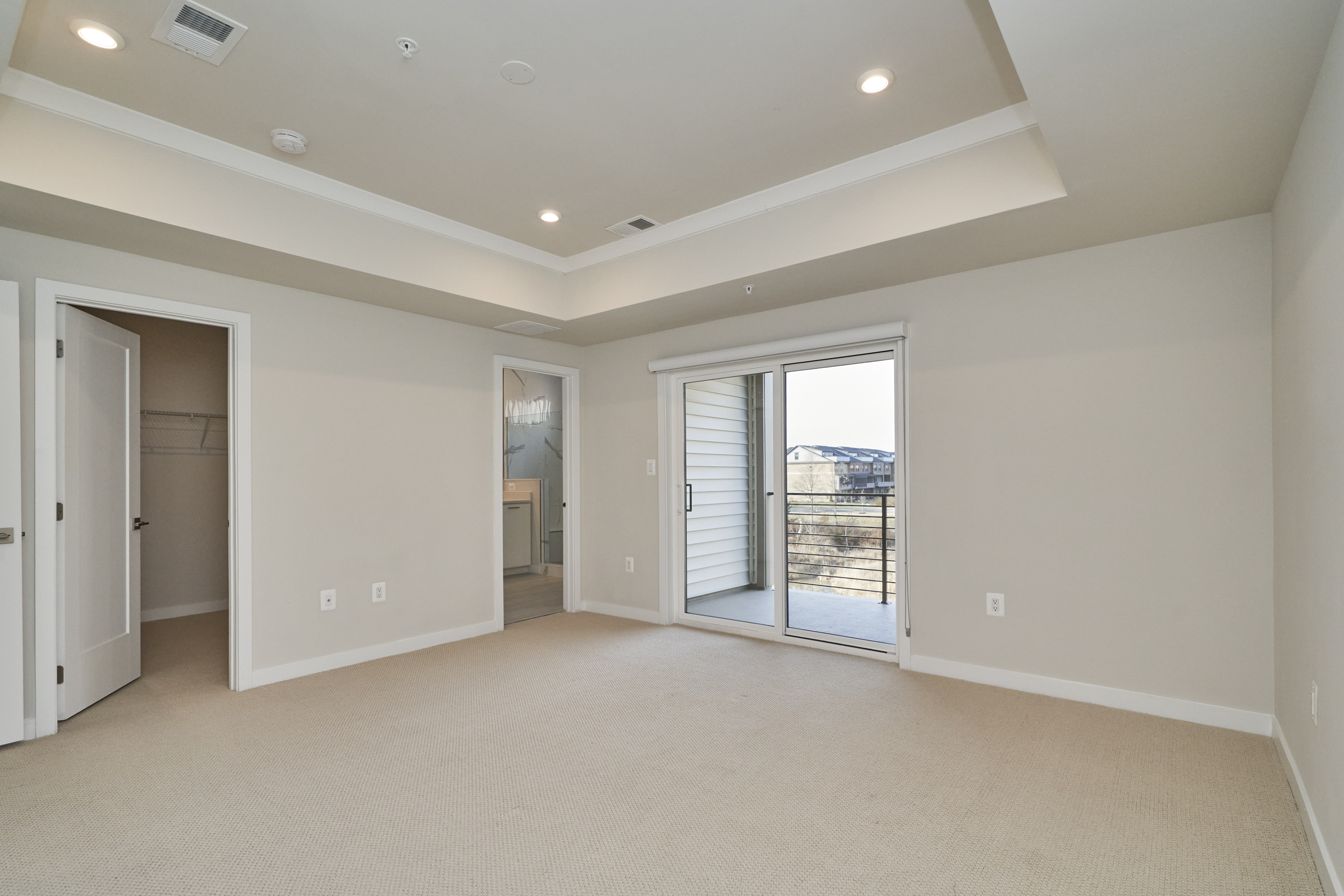 Interior professional photo of 43522 Centergate Drive - showing the primary bedroom with deep trey ceiling and view out to the balcony and walk in closet