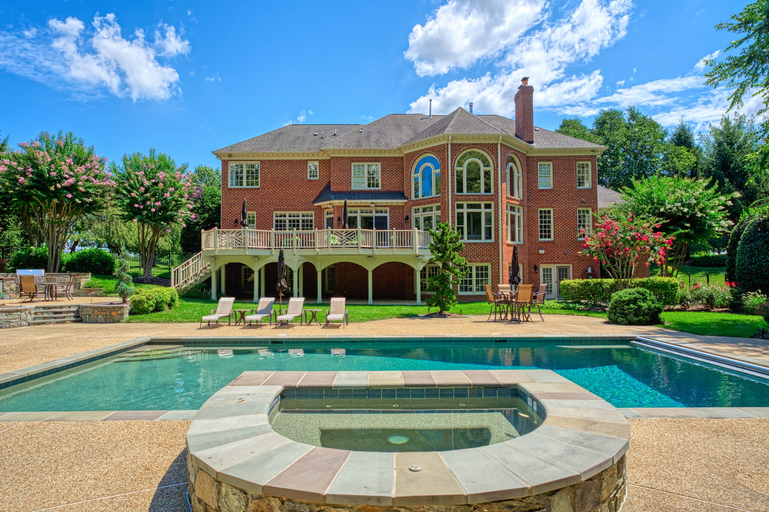 Professional exterior photo of 17087 Bold Venture Drive, Leesburg - showing the rear of the home with large deck, several stone patios and pool and hot tub in the foreground