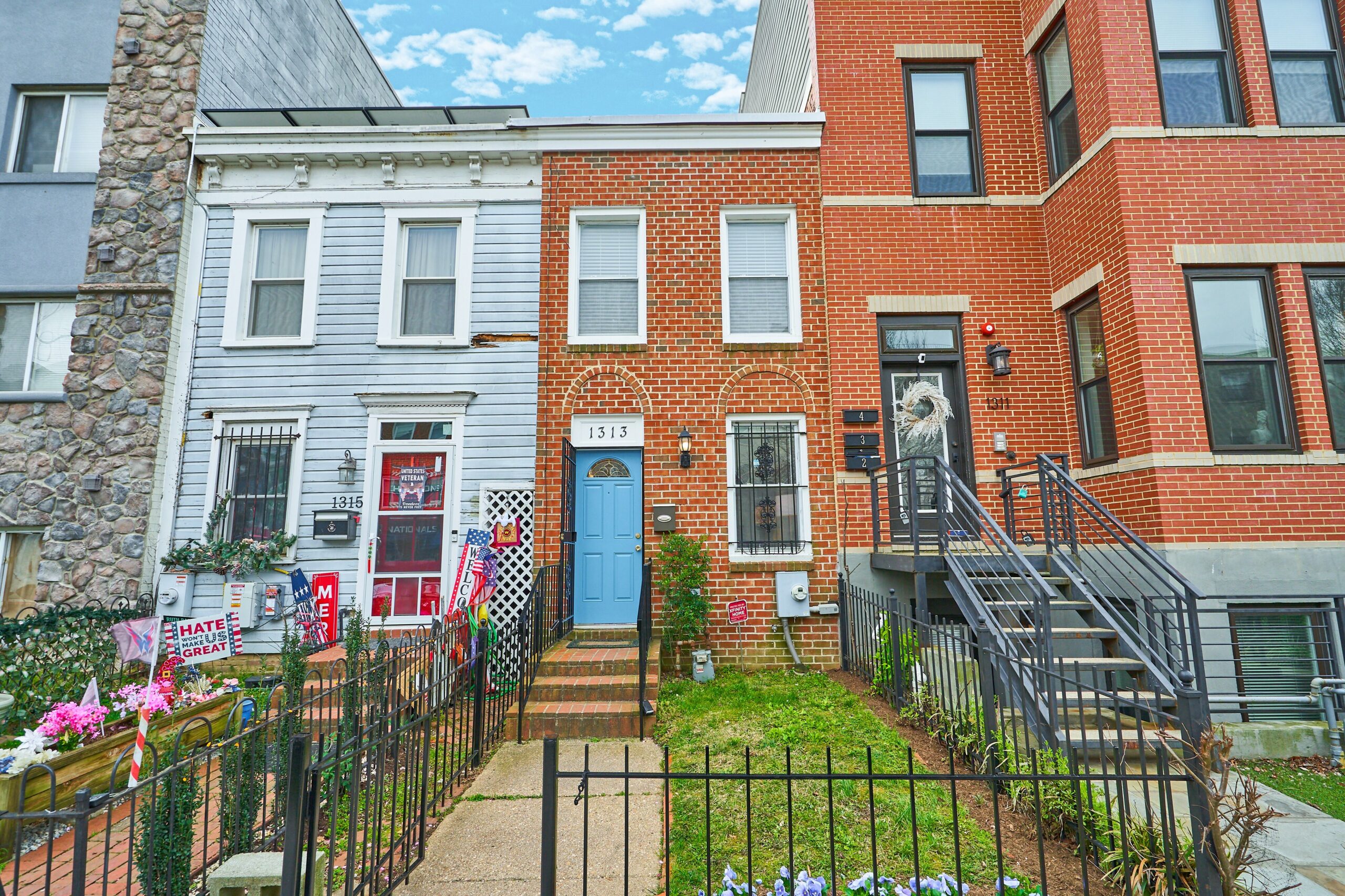 Professional exterior photo of 1313 K Street SE, Washington, DC - showing a brick-front 2-story townhome with fenced in front garden and entrance and sky blue front door