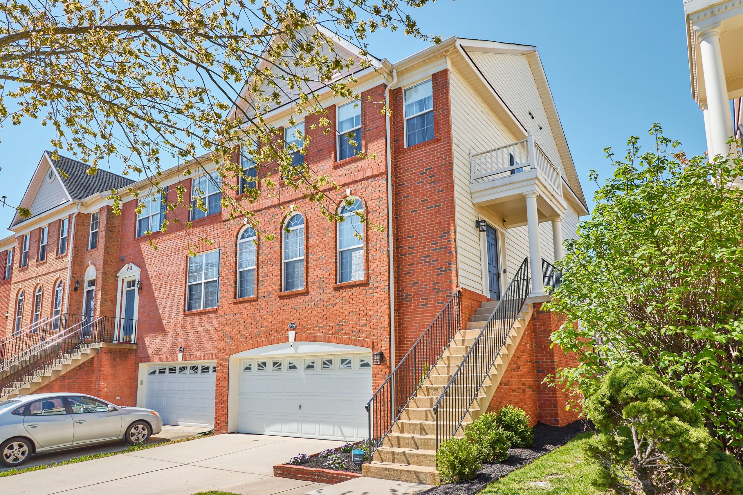 Professional exterior photo of 25499 Beresford Drive, Chantilly, Virginia - showing brick-front end unit townhome wish 2 car garage, 3 stories and side stairway entrance