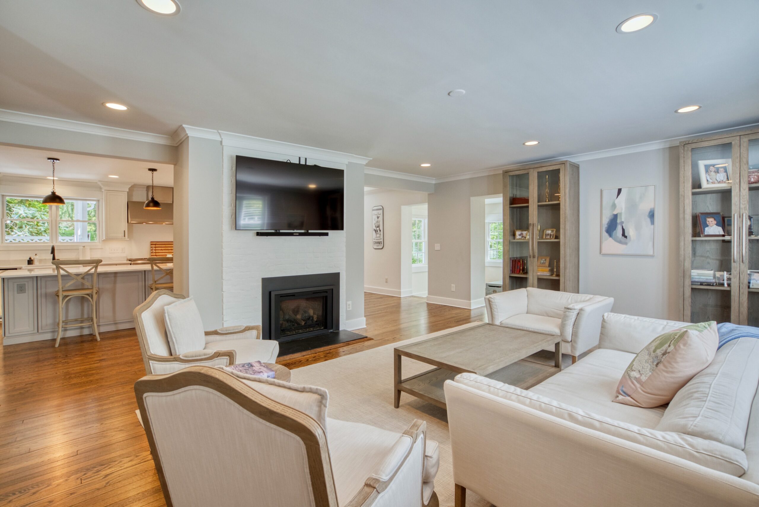 Professional interior photo of 209 Norwood Road, Annapolis, MD - showing the formal living room with fireplace and mounted TV on a wide pillar that flows into the kitchen visible beyond