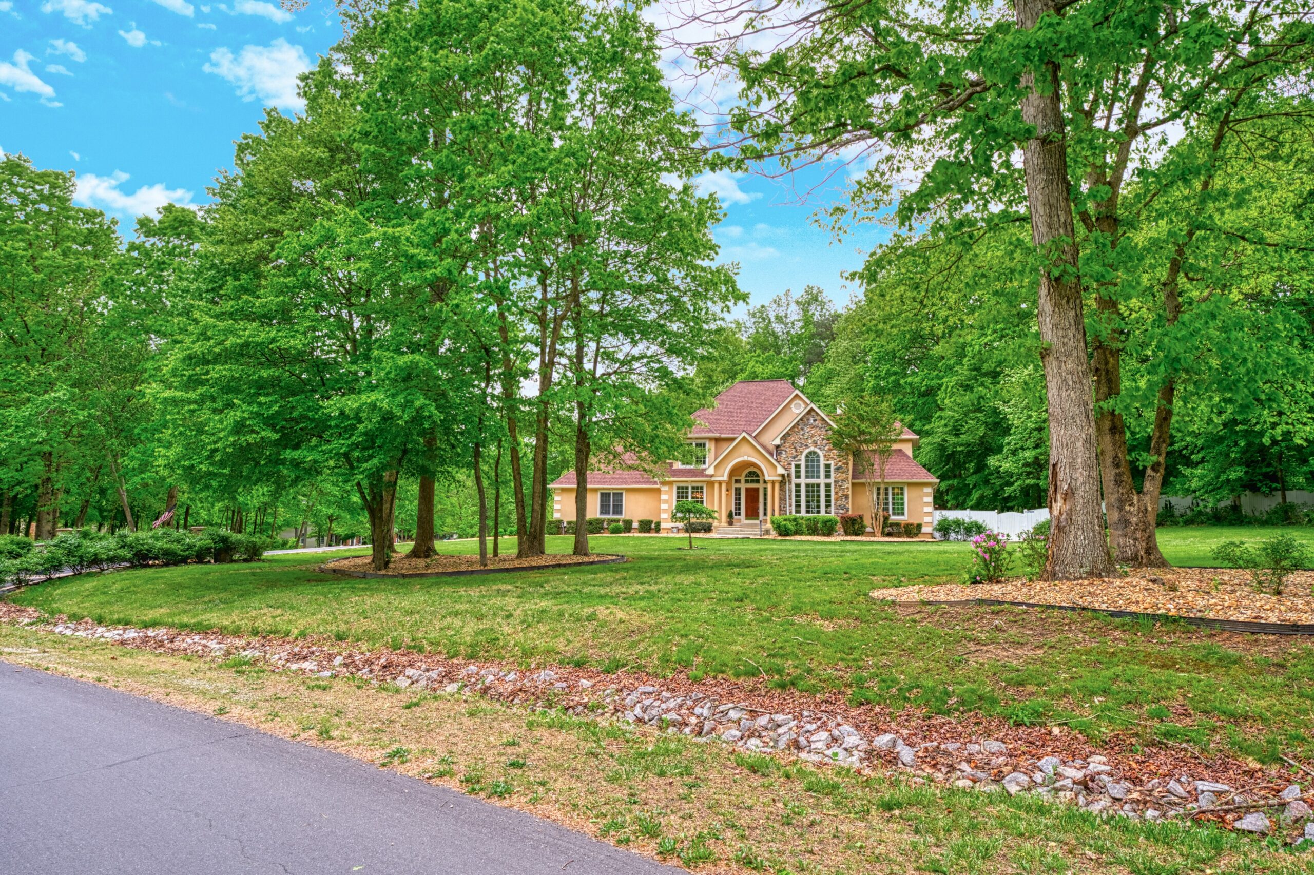 Professional exterior photo of 13700 Holly Forest Dr - from the road showing the front from across the yard, a French countryside style estate home surrounded by mature trees at the back
