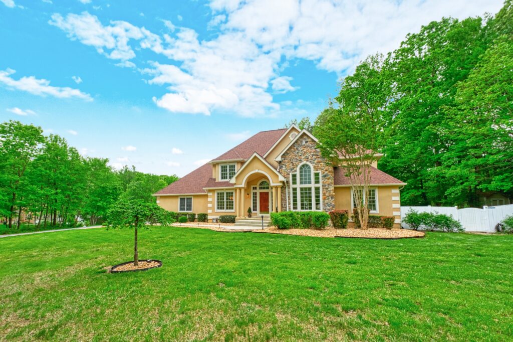 Professional exterior photo of 13700 Holly Forest Dr - showing the front from across the yard, a French countryside style estate home surrounded by mature trees at the back
